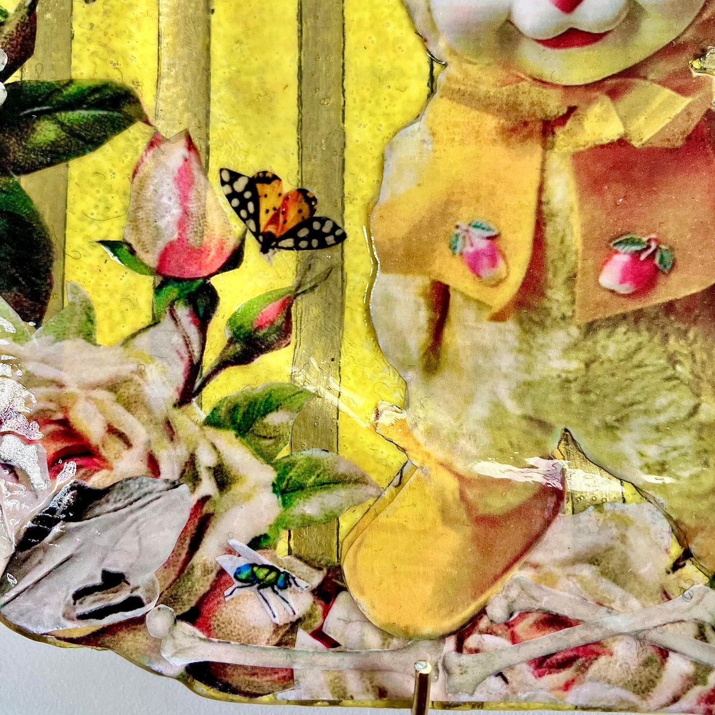"Not Seeking Anyone's Approval" Wall Plate by House of Frisson, closeup detail of the collage showing a kitsch vintage bunny toy, roses, bones, moths, on a yellow and gold striped background.