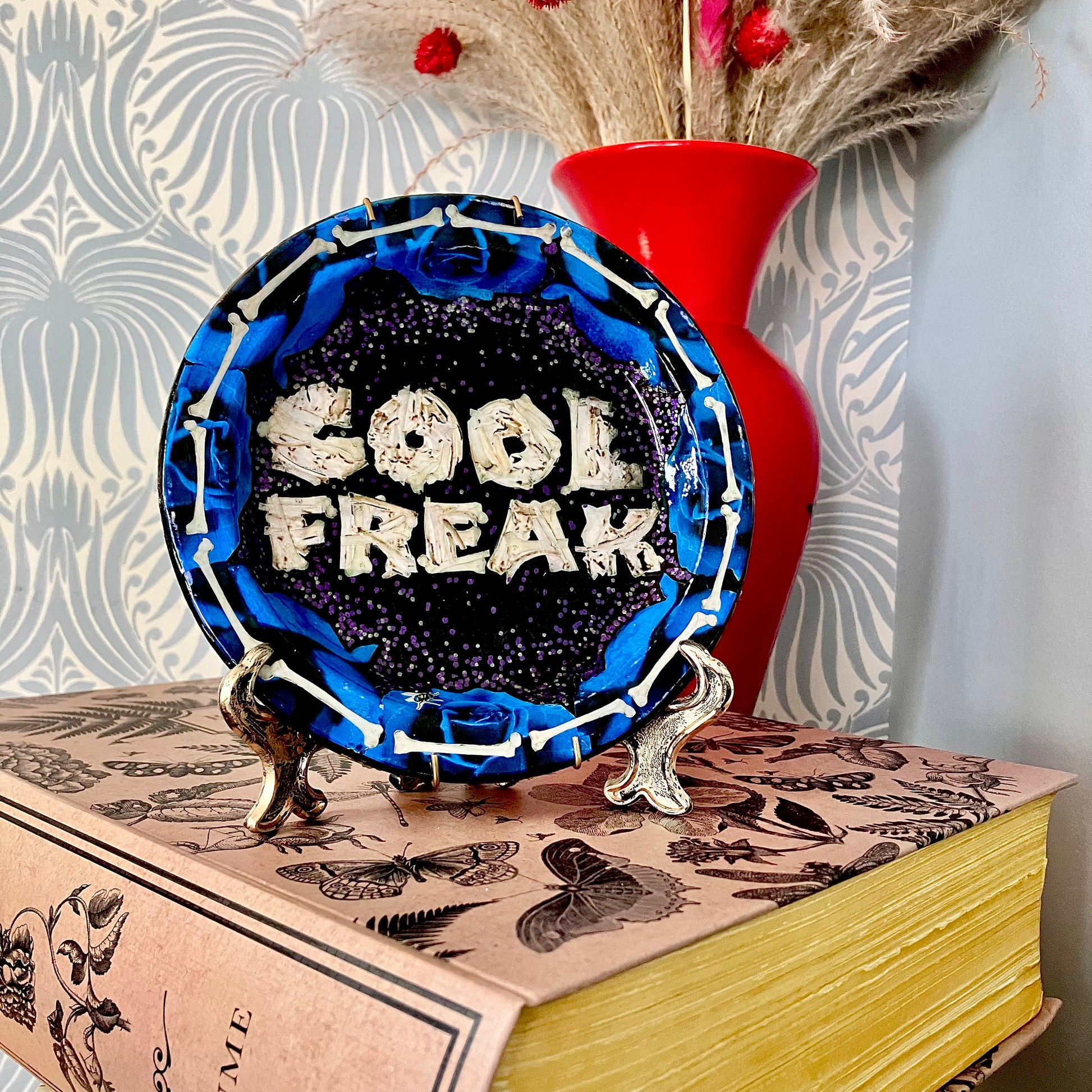 "Cool Freak" Wall Plate by House of Frisson lifestyle photo of the plate on a plate stand, resting on a book.