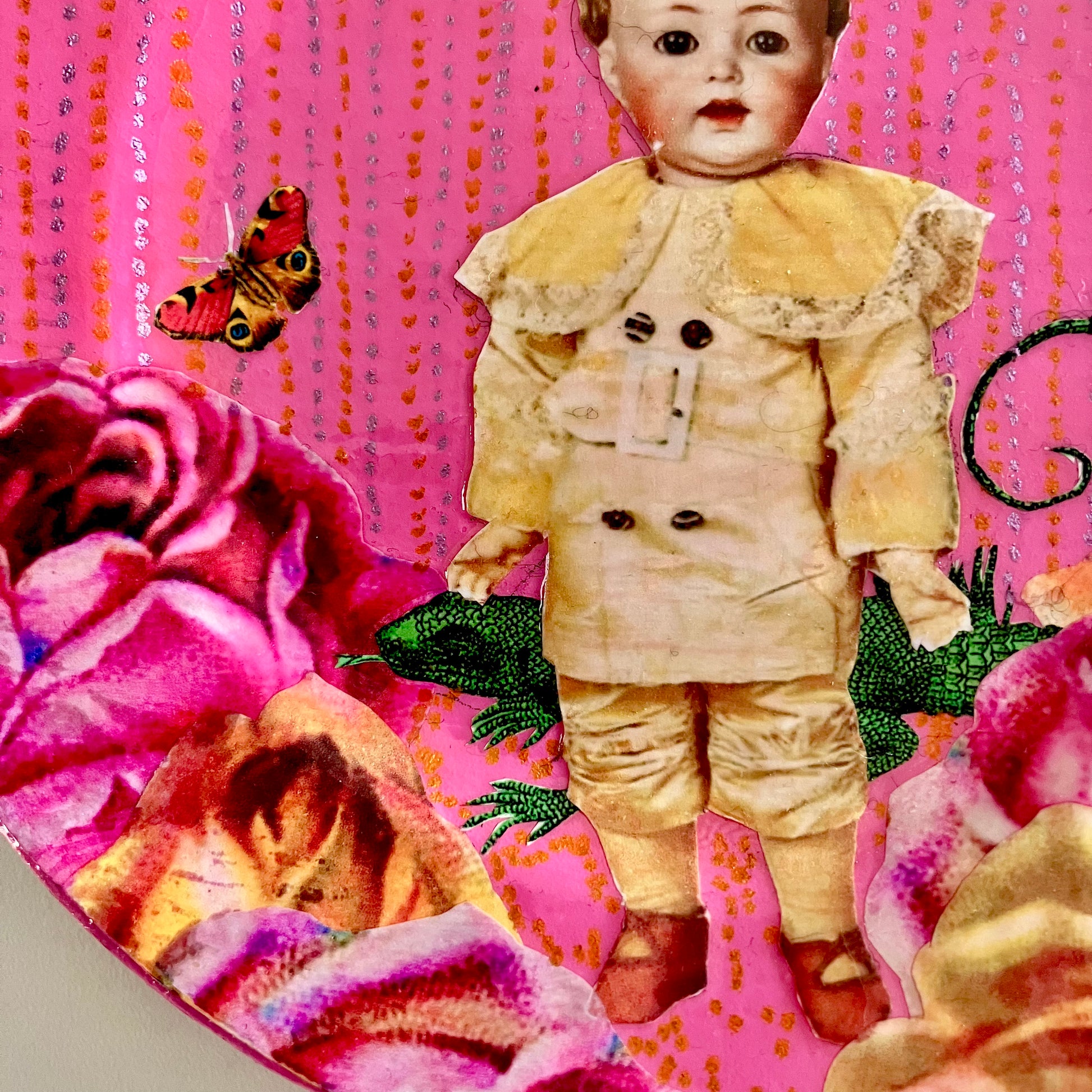 Against Conformity Wall Plate by House of Frisson, closeup detail of the collage, showing a kitsch vintage male doll, some roses, a lizard, and a moth, on a pink coloured background.