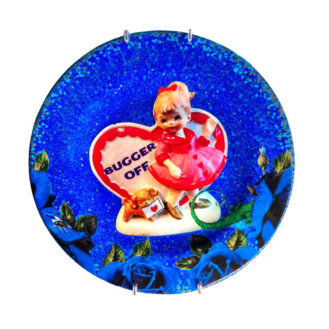 "Bugger Off" blue Wall Plate by House of Frisson, featuring a kitsch vintage porcelain figure among blue roses and a lizard and a fly.