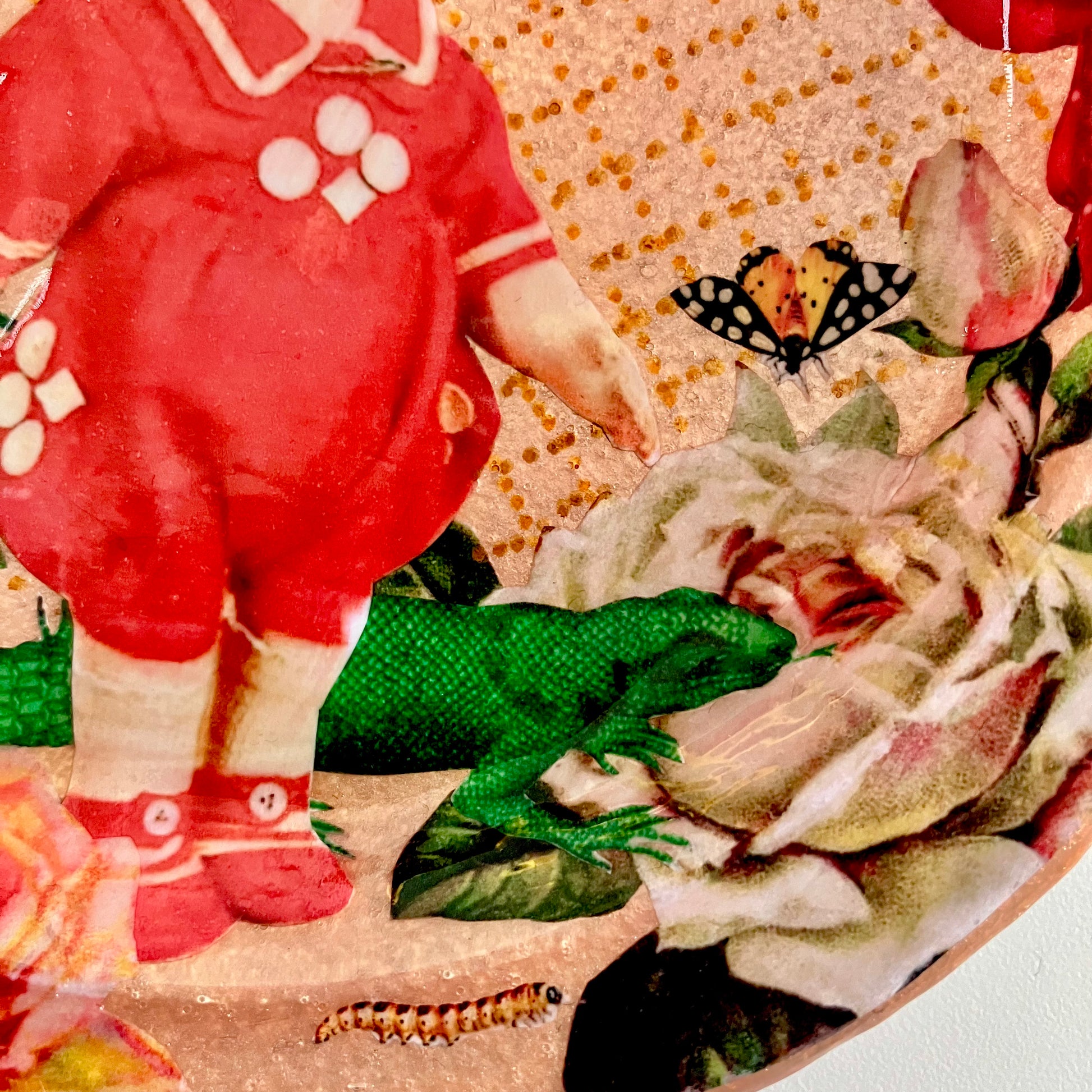 Chaos, Bliss, and Sweet Ecstasy Wall Plate by House of Frisson, closeup detail of the collage showing a vintage doll, a lizard, a moth, and roses, on a blush coloured background.