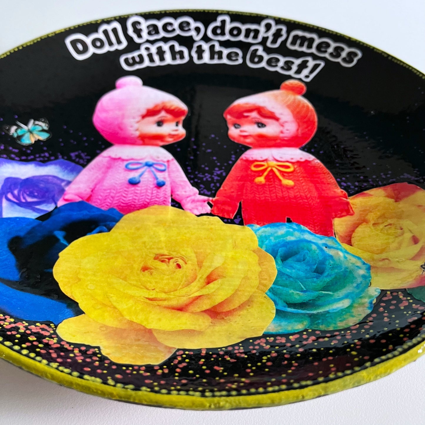 Black Upcycled Wall Plate featuring two vintage rubber dolls, surrounded by colourful roses, and a cheeky quote. Showing details of the collage.