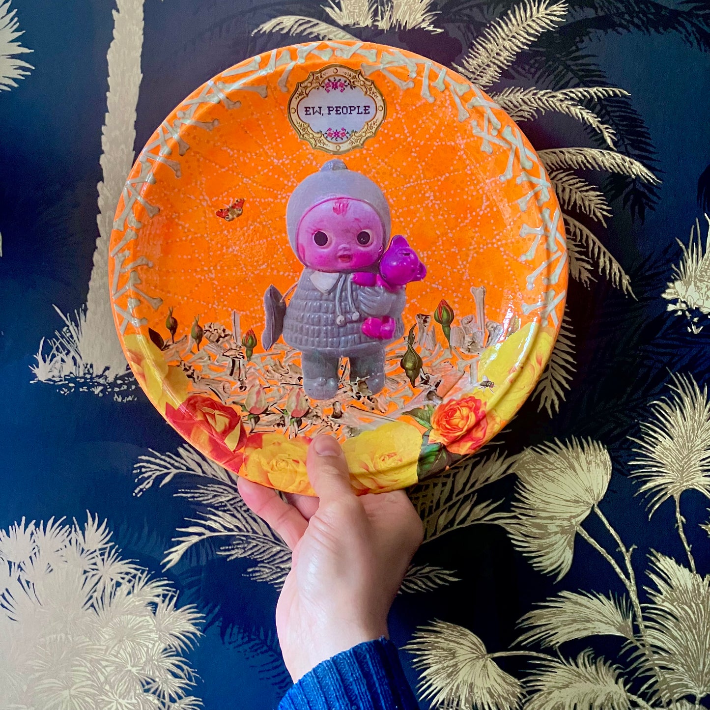 Neon orange wall plate by House of Frisson, featuring a vintage doll surrounded by bones and flowers, this plate exclaims "Ew, People" to poke fun at those who find dolls creepy. Plate o hand.