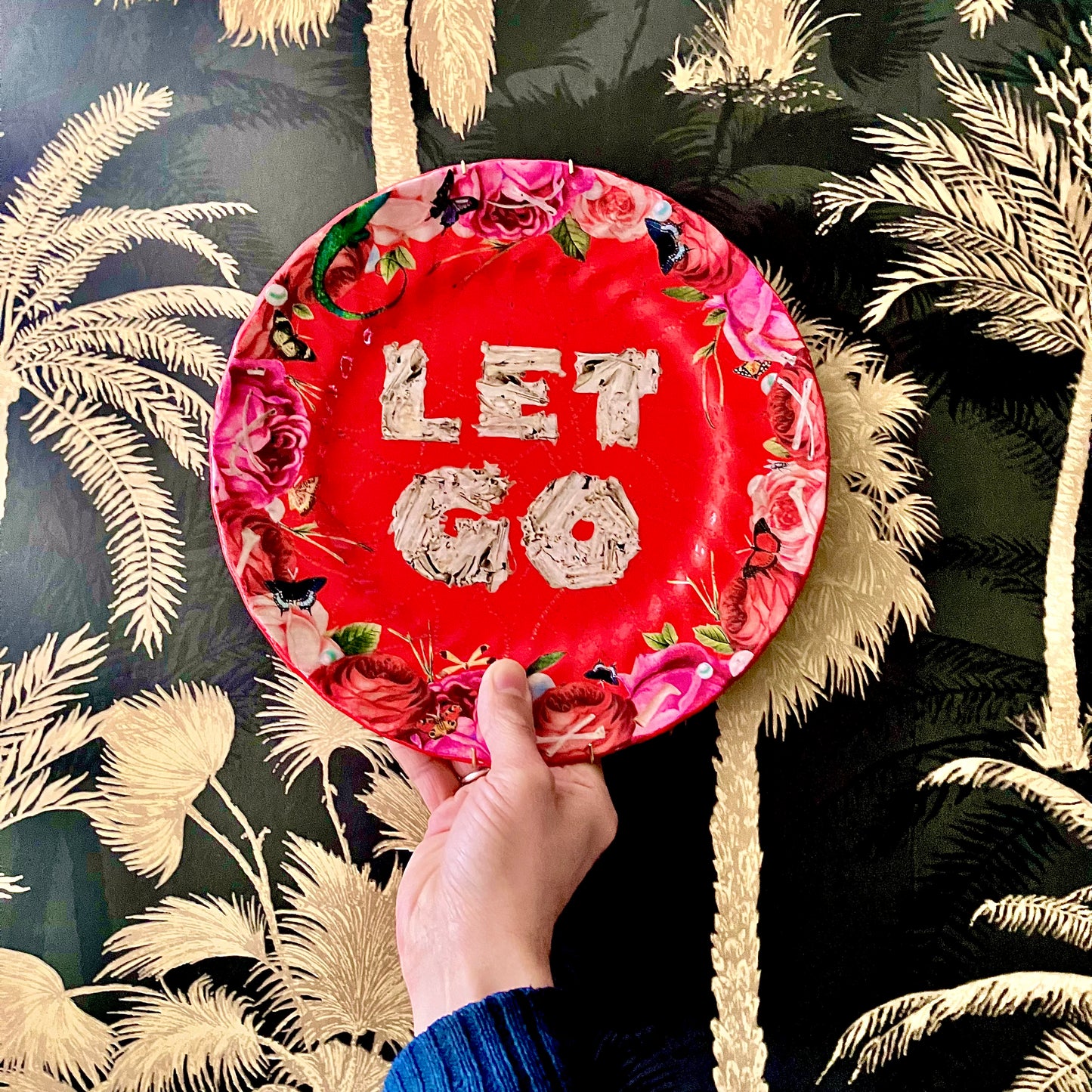 "Let Go" Wall Plate by House of Frisson on hand against a wallpaper.