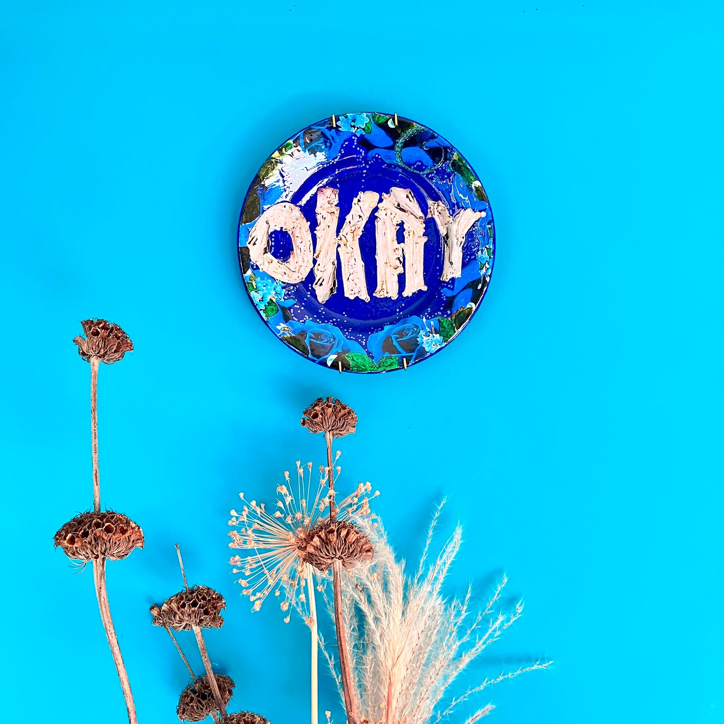 House of Frisson's "Okay" Wall Plate one-of-a-kind collage artwork on up-cycled plate. Plate hanging on a blue wall.