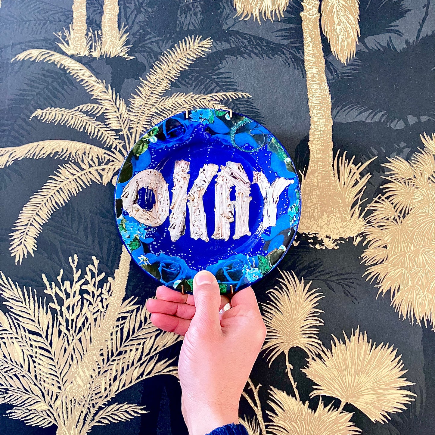 House of Frisson's "Okay" Wall Plate one-of-a-kind collage artwork on up-cycled plate. Holding the plate against a wallpaper.