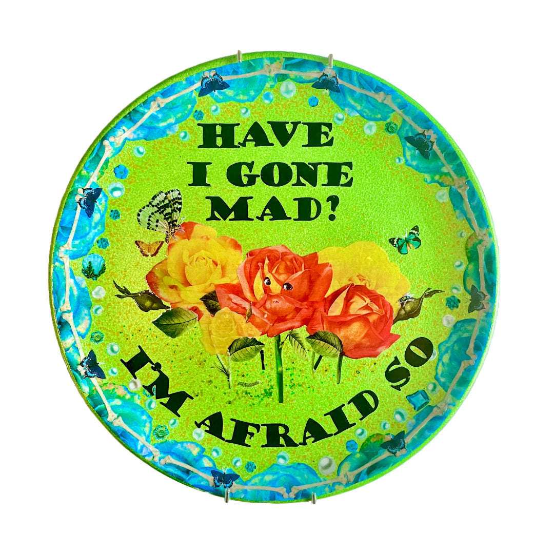"Have I Gone Mad? I'm Afraid So" Wall Plate by House of Frisson, featuring a collage artwork of roses with faces, framed by blue roses, blue moths, pearls, and bones, against a bright green background.