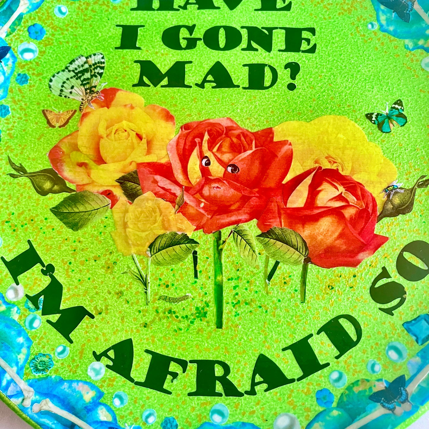 "Have I Gone Mad? I'm Afraid So" Wall Plate by House of Frisson closeup detail of the collage showing roses with faces, against a bright green background.