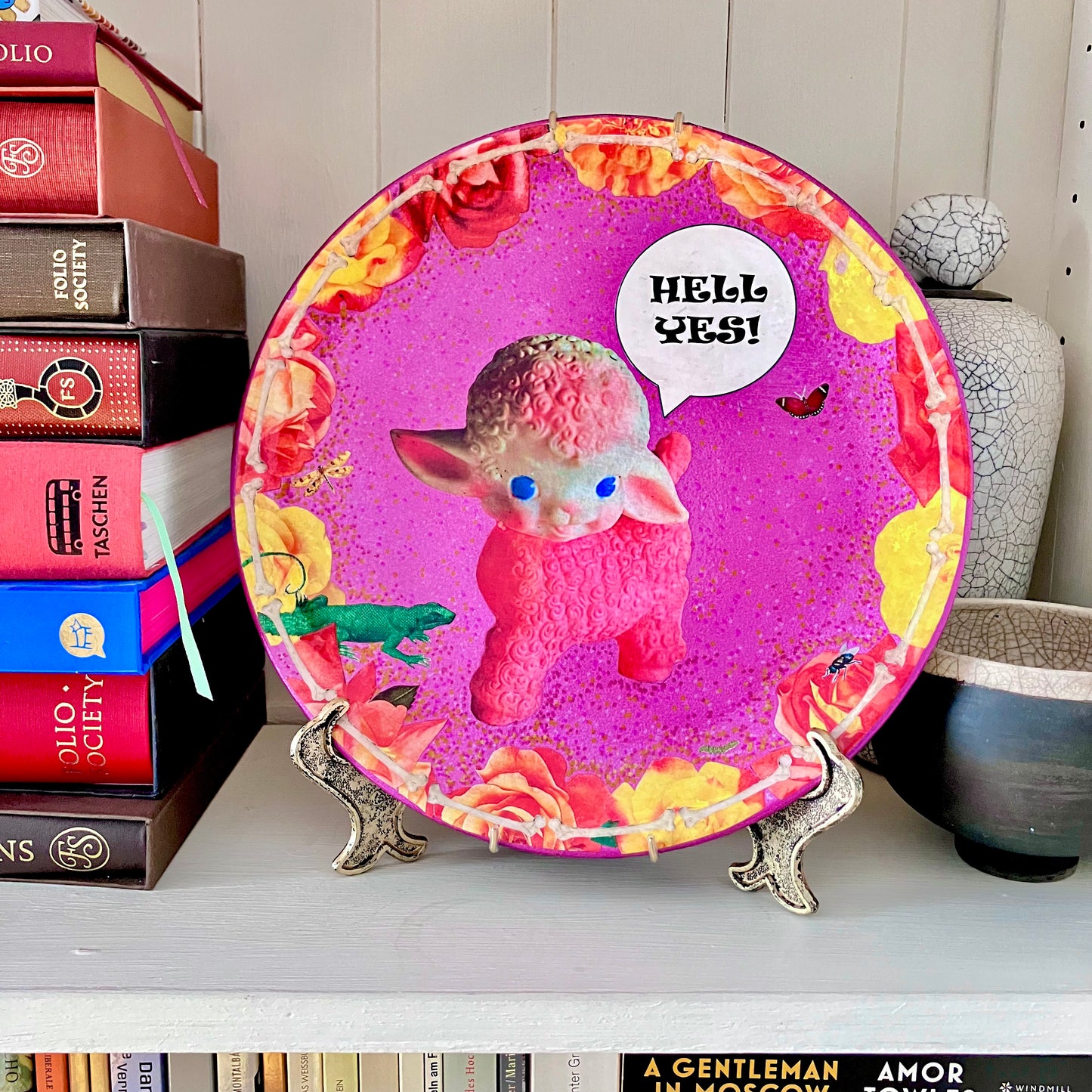"Hell Yes" Wall Plate by House of Frisson on a plate stand resting on a bookshelf.
