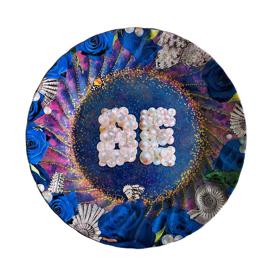 "Be" Wall Plate by House of Frisson. Featuring a collage with the word "Be" written with pearls, framed by blue roses, pearls, shells, and moths, on a blue background with golden details.