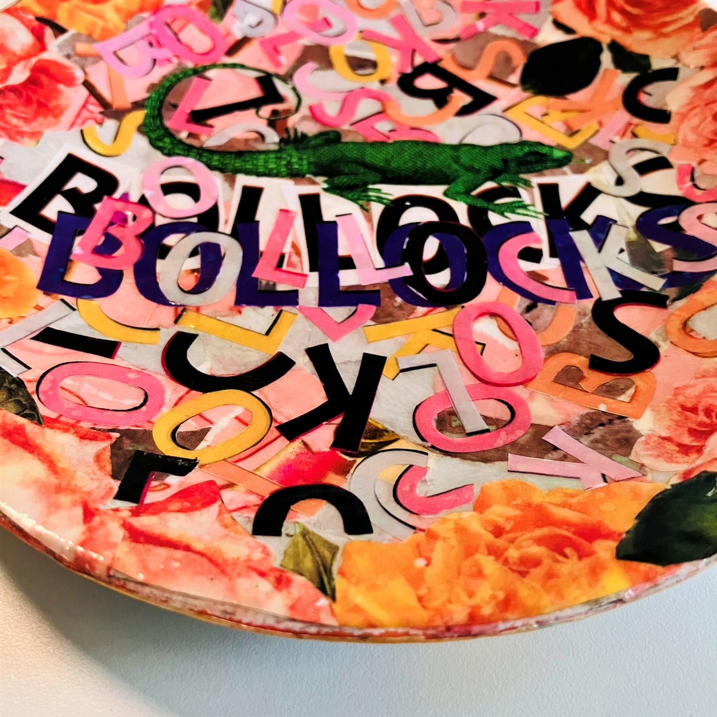 "Bollocks" Wall Plate by House of Frisson, featuring a collage of colourful letters forming the word "bollocks", and a lizard, framed by roses. Closeup detail showing the colourful letters.
