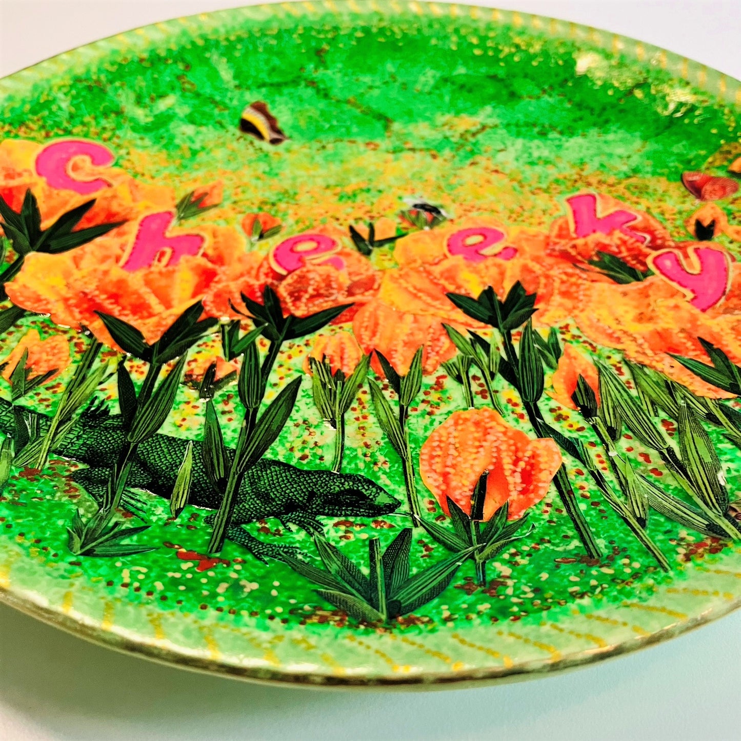"Cheeky" Wall Plate by House of Frisson, featuring a collage with letters coming out of flowers forming the word "cheeky", and a lizard, on a green background. Closeup detail showing a lizard between the flowers.
