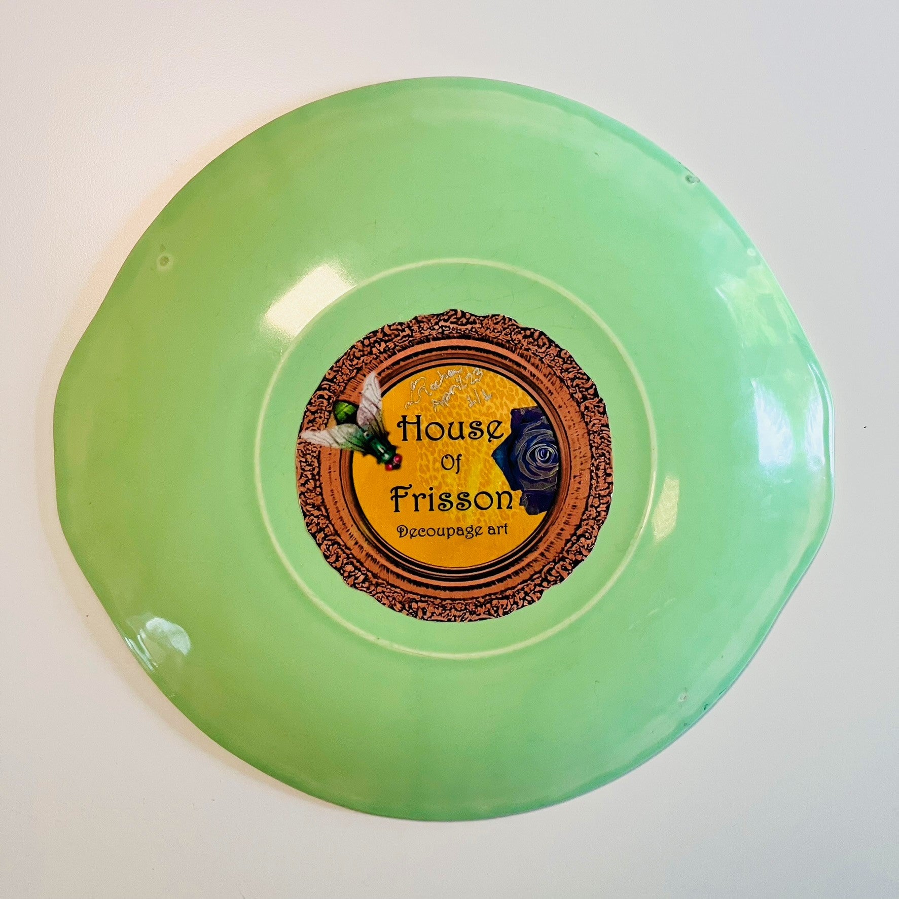 "Cheeky" Wall Plate by House of Frisson, featuring a collage with letters coming out of flowers forming the word "cheeky", and a lizard, on a green background. Showing back of the plate.