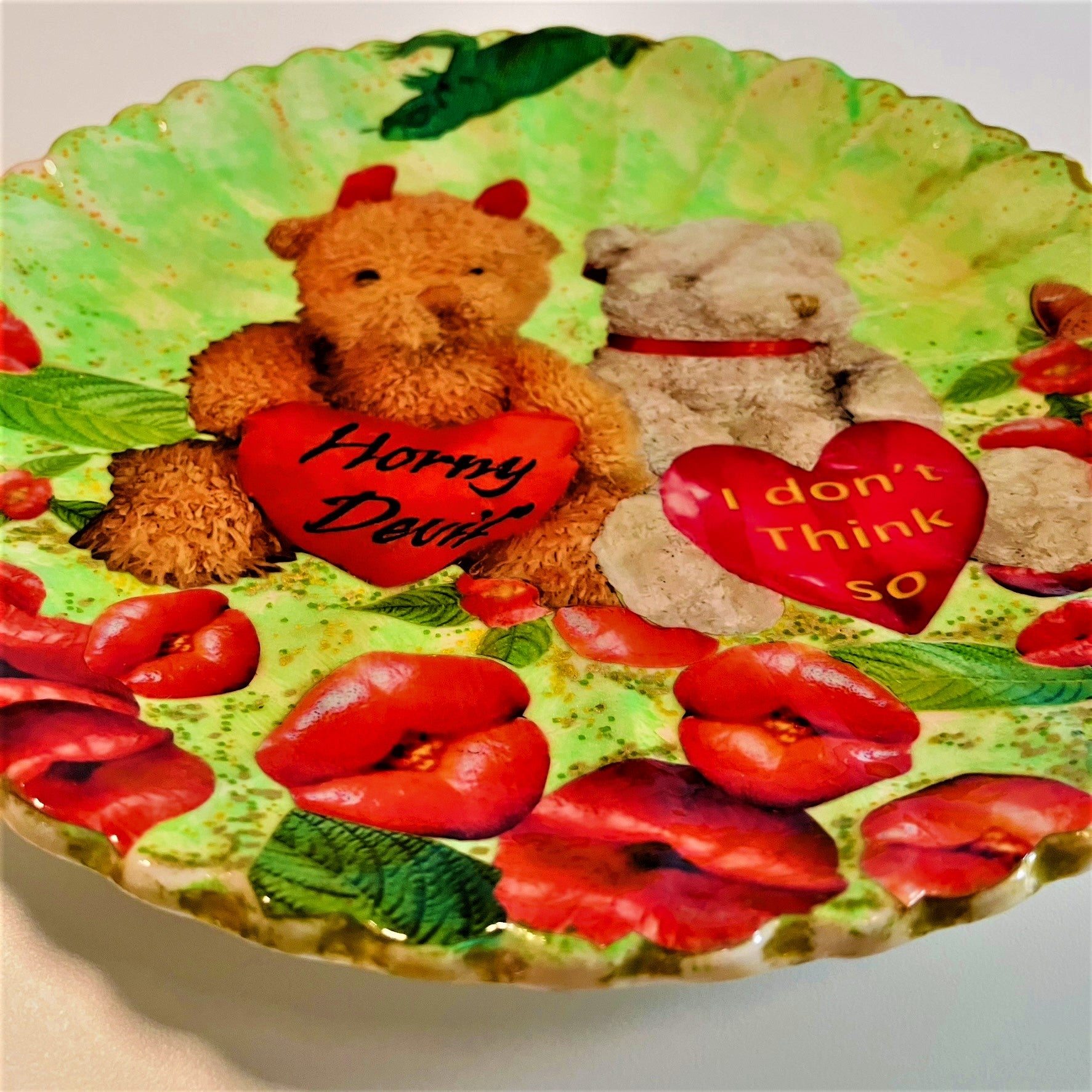 "Horny Devil. I Don't Think So" Wall Plate by House of Frisson, featuring a collage of two teddy bears holding hearts with messages, among lip-shaped flowers, on a green background. Closeup detail showing the lip-shaped flowers.
