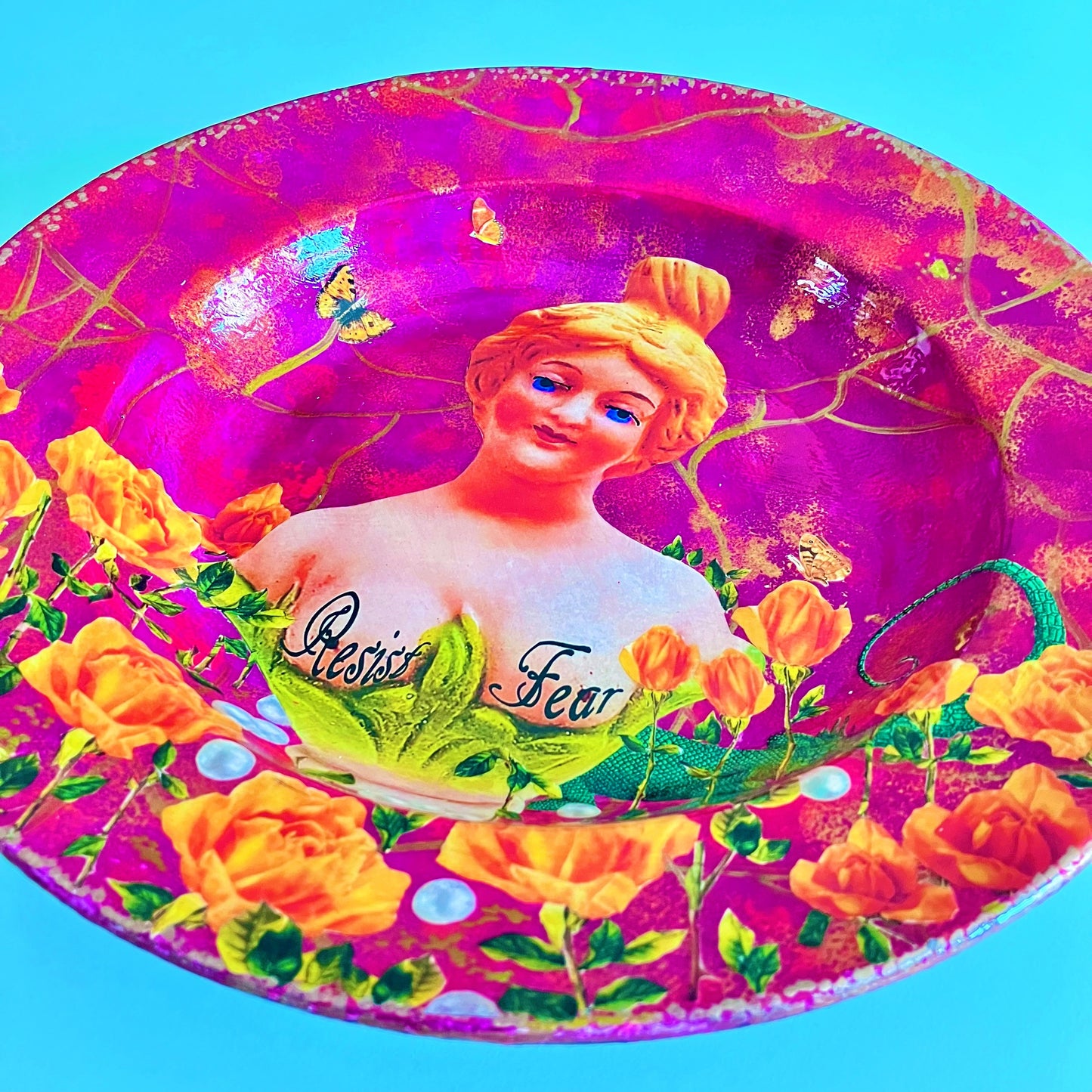 "Resist Fear" Wall Plate by House of Frisson, featuring a female bust statue with "Resist Fear" written across breasts, surrounded by flowers, and pearls, on a purple background. Closeup details showing flowers, pearls, and a lizard.