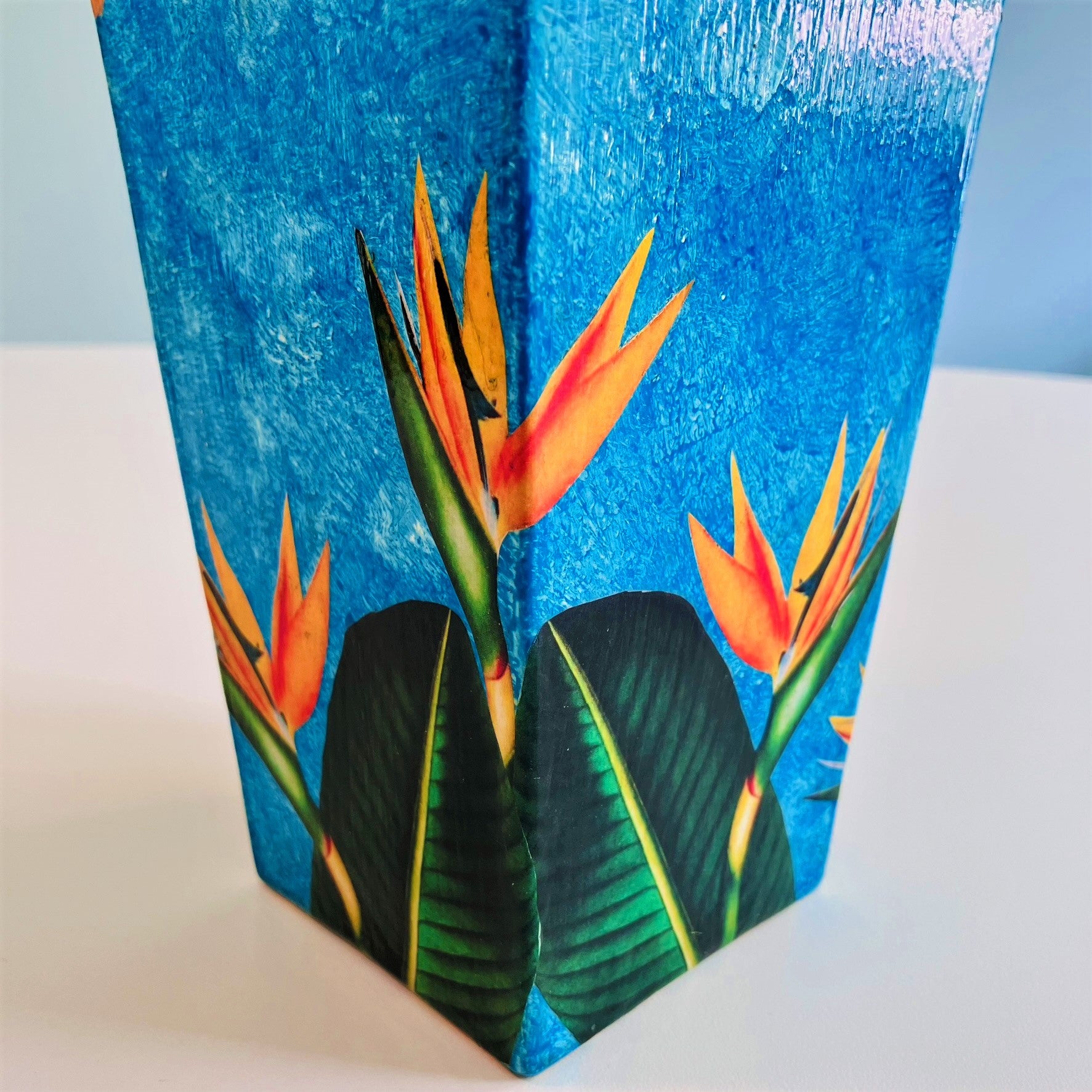 "Strelitzia" Flower Vase by House of Frisson, featuring strelitzia flowers and leaves, on a blue and golden background. Showing detail of the flowers.