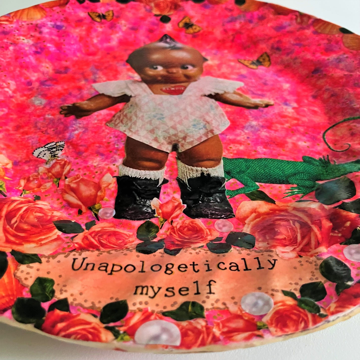 "Unapologetically Myself" Wall Plate by House of Frisson, featuring a vintage black doll surrounded by roses , pearls, moths, and a lizard, framed by shells, on a pink background. Showing closeup details of the roses and pearls.