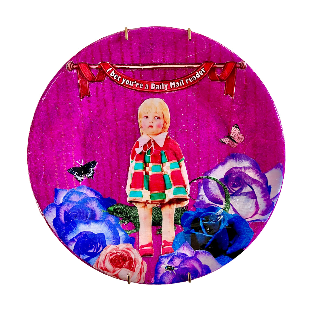 "I Bet You're A Daily Mail Reader" Wall Plate by House of Frisson, featuring a collage artwork of a kitsch vintage doll, surrounded by blue roses, moths, and a lizard, on a purple background.