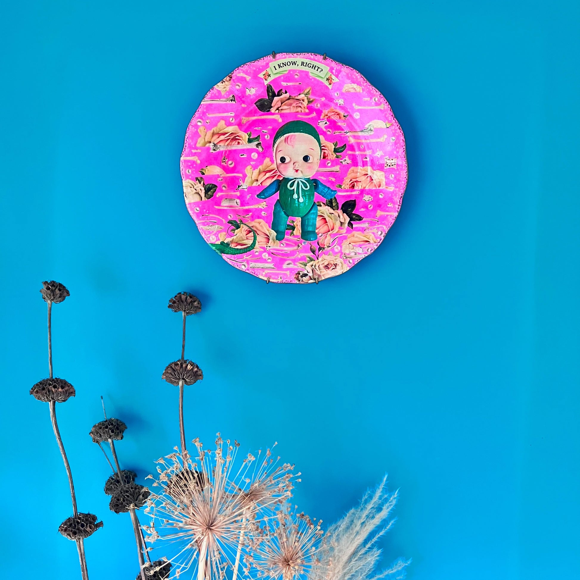 Neon Pink Upcycled Wall Plate featuring a collage of a vintage celluloid doll on a pattern of roses, bones, and pearls. 