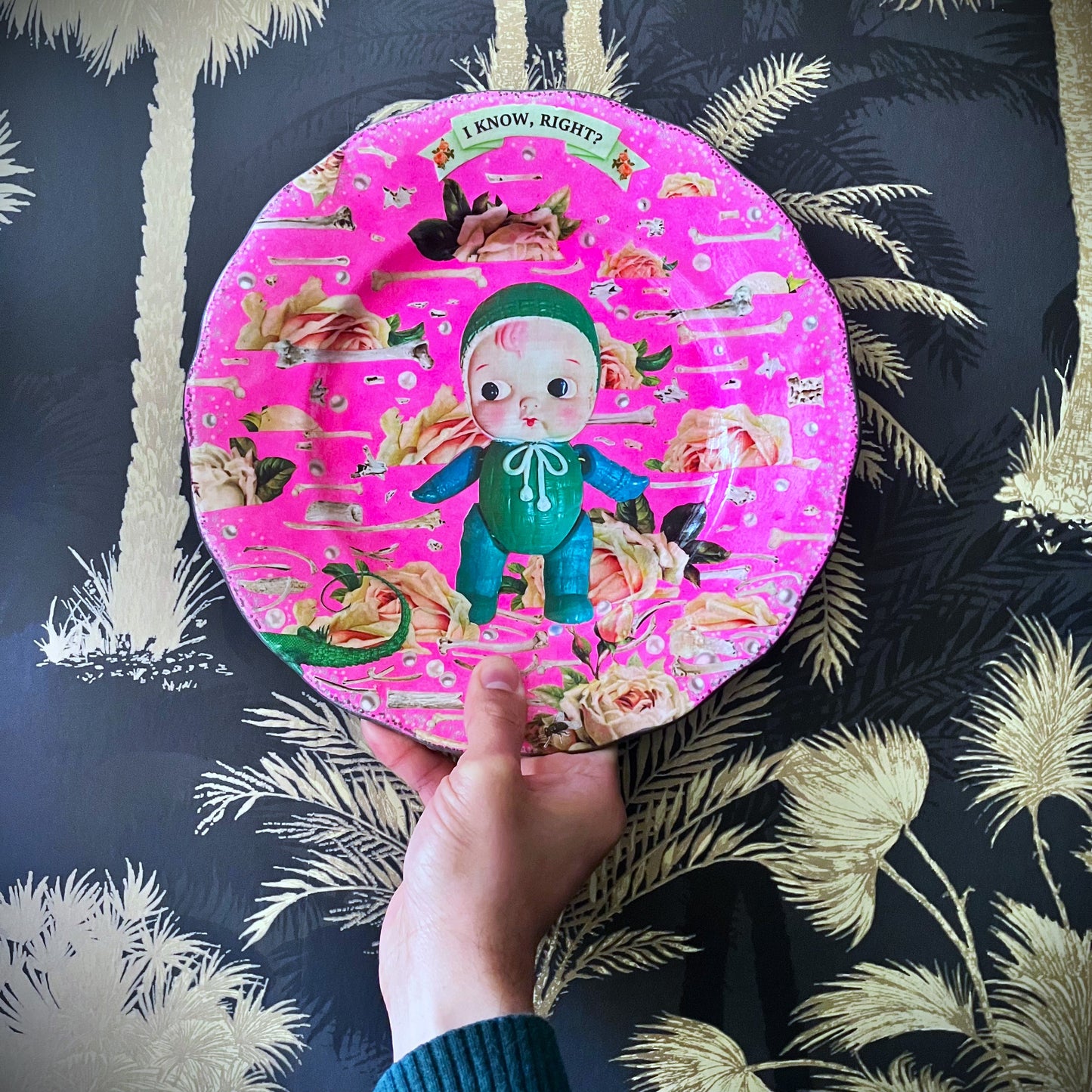 Neon Pink Upcycled Wall Plate featuring a collage of a vintage celluloid doll on a pattern of roses, bones, and pearls. 