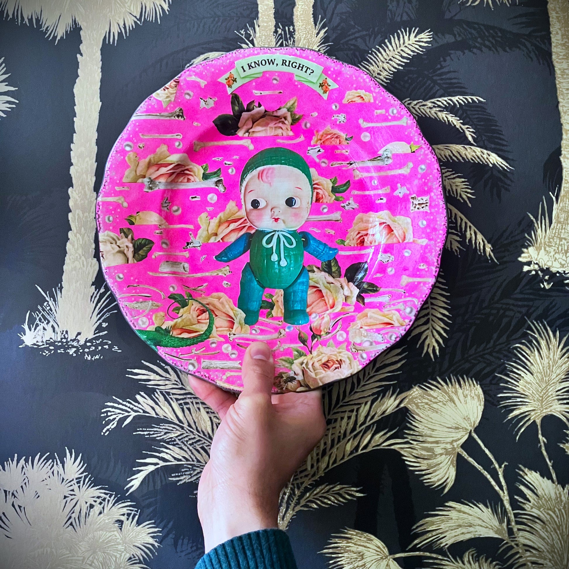 Neon Pink Upcycled Wall Plate featuring a collage of a vintage celluloid doll on a pattern of roses, bones, and pearls. 