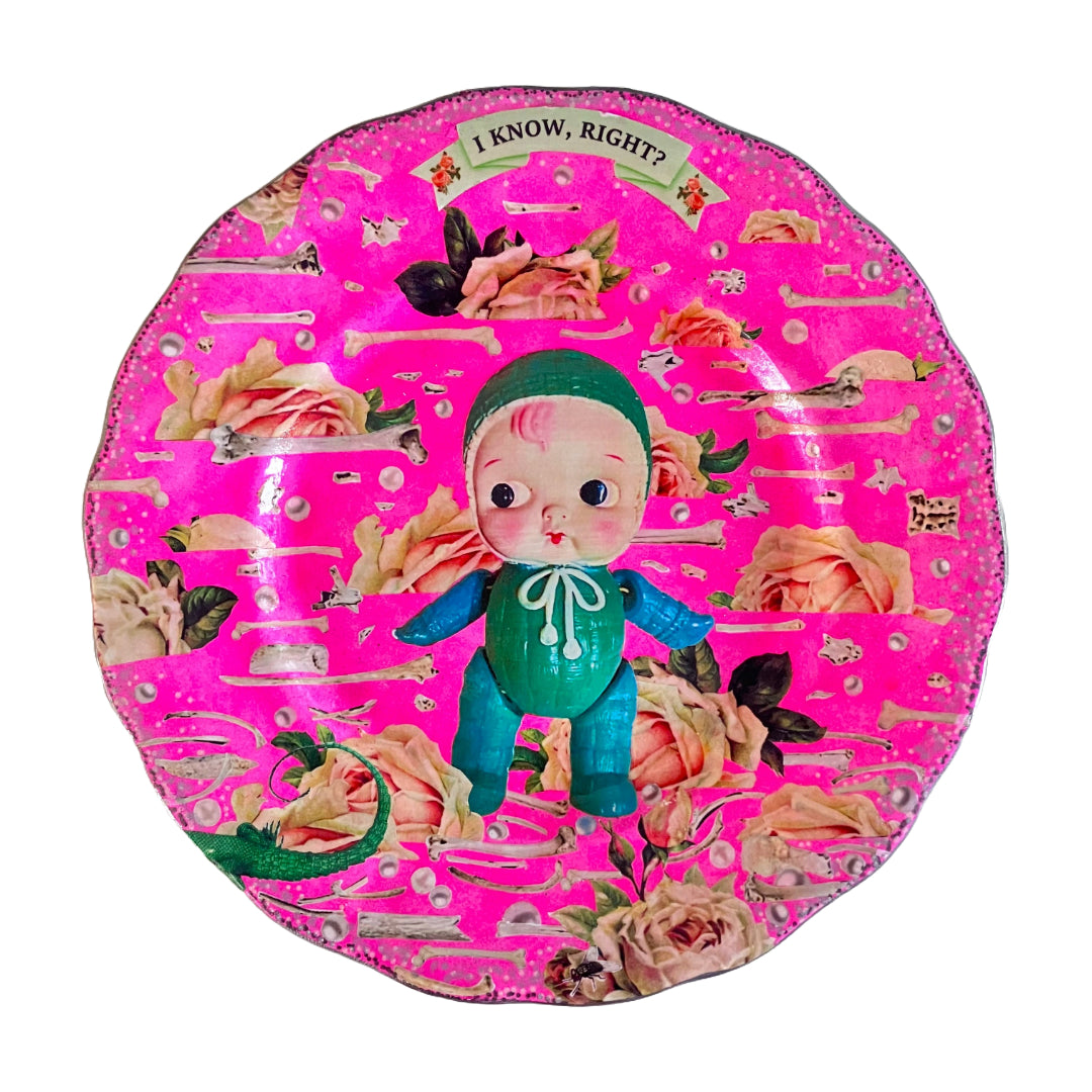 Neon Pink Upcycled Wall Plate featuring a collage of a vintage celluloid doll on a pattern of roses, bones, and pearls. 