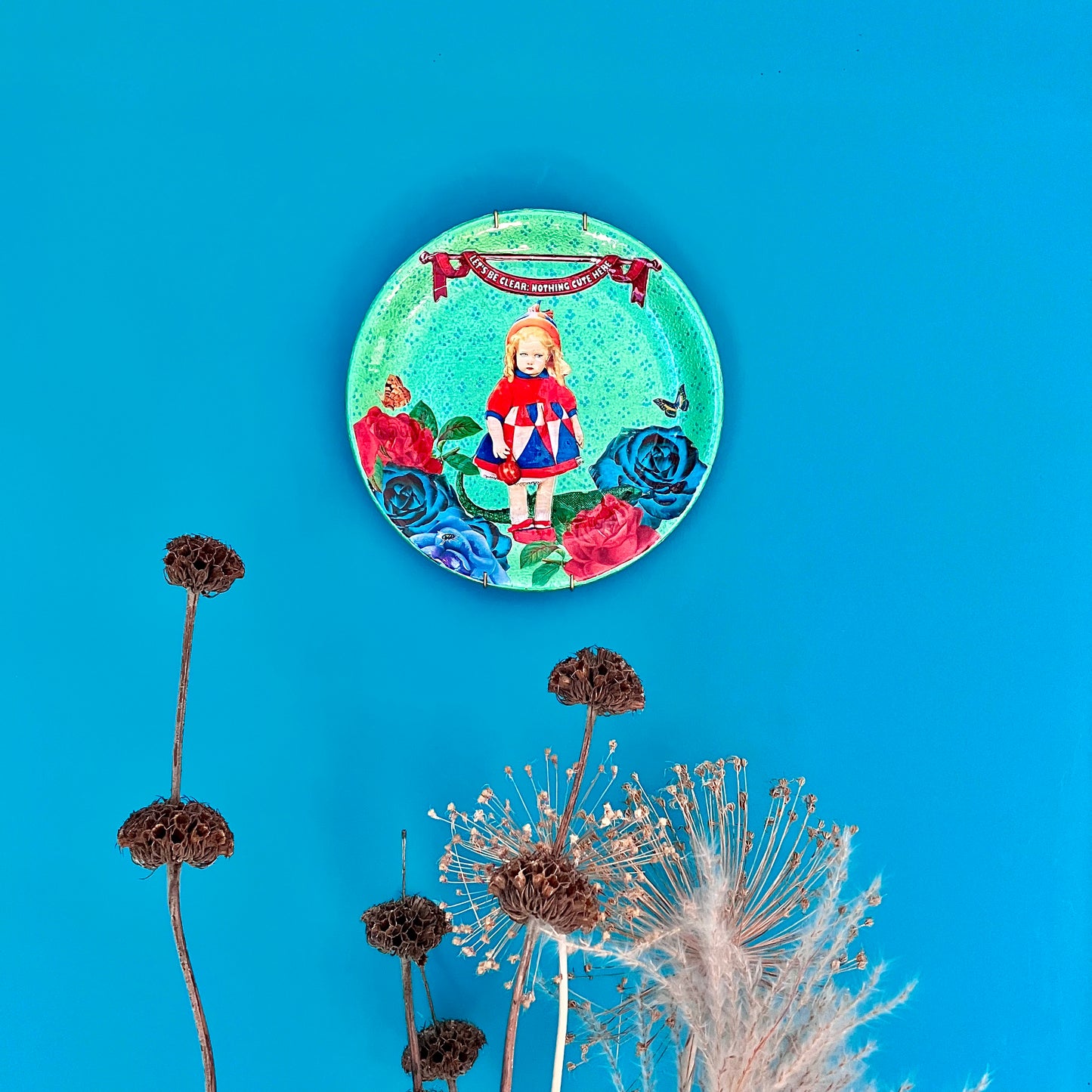 "Let's Be Clear: Nothing Cute Here" Wall Plate by House of Frisson, hanging on a blue wall.