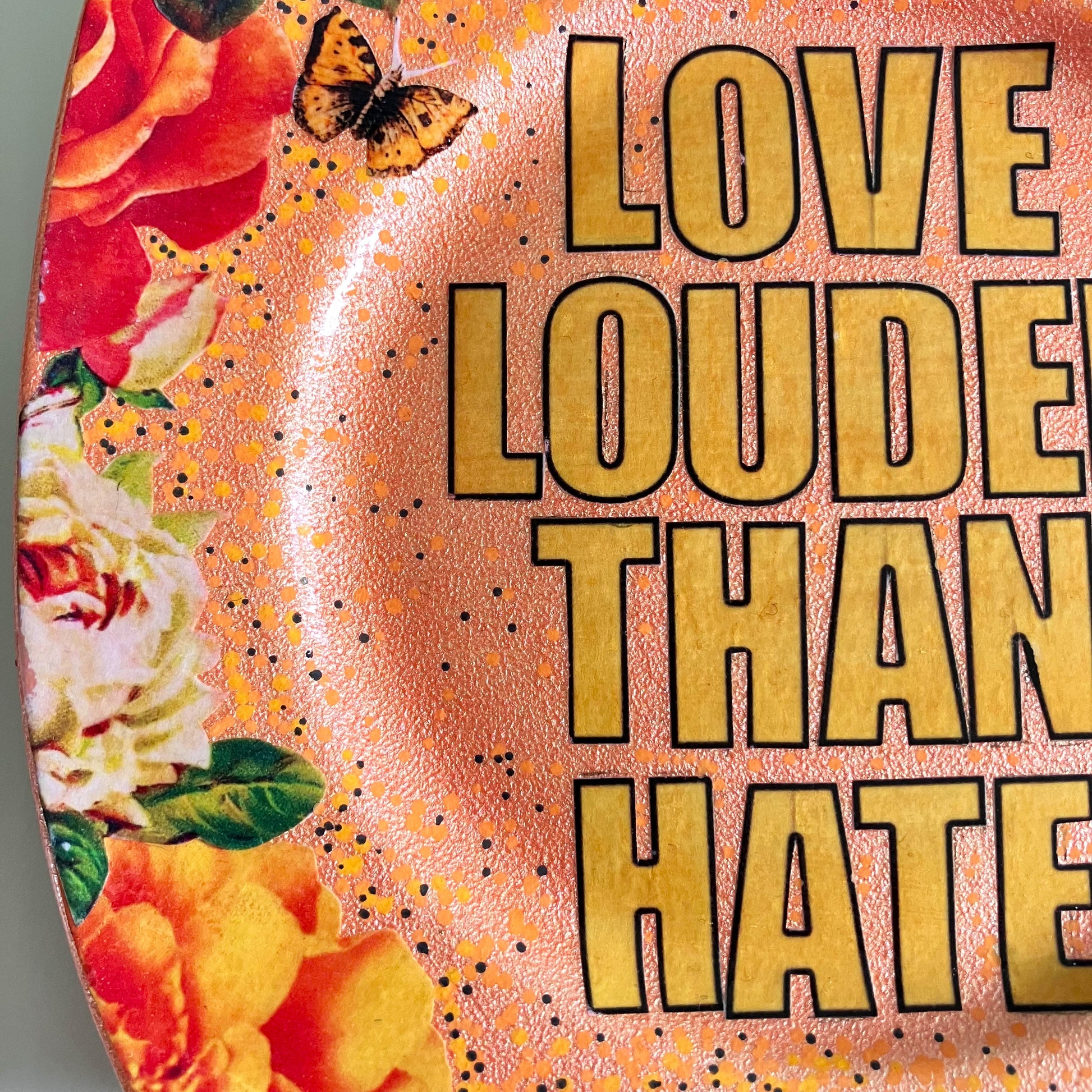 "Love Louder Than Hate" Upcycled Wall Plate by House of Frisson, featuring a collage of the words "love louder than hate" set against a peach background and framed by roses. Closeup details showing the collage artwork.