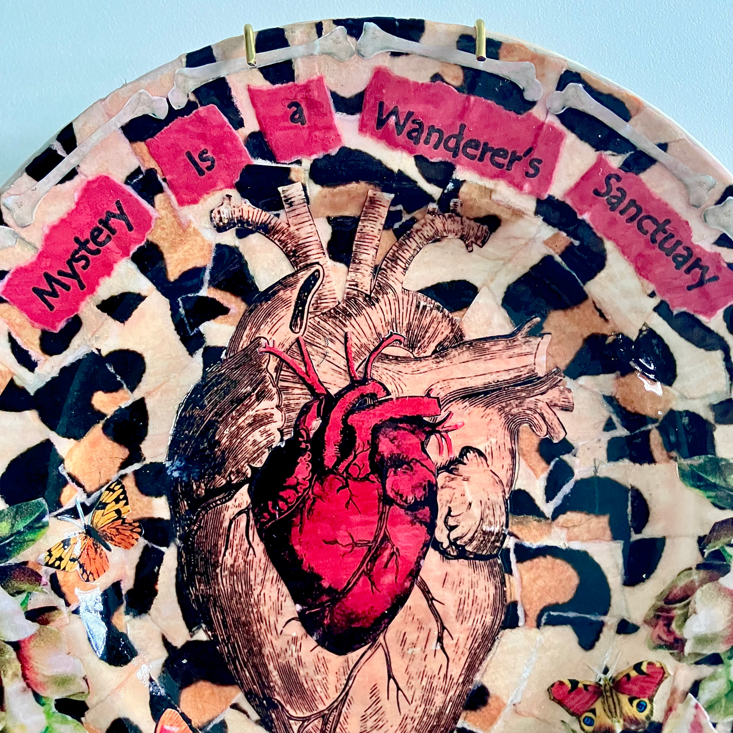 Mystery is a Wanderer's Sanctuary Wall Plate by House of Frisson, closeup detail of the collage showing two anatomical human heart illustrations against a leopard print pattern.