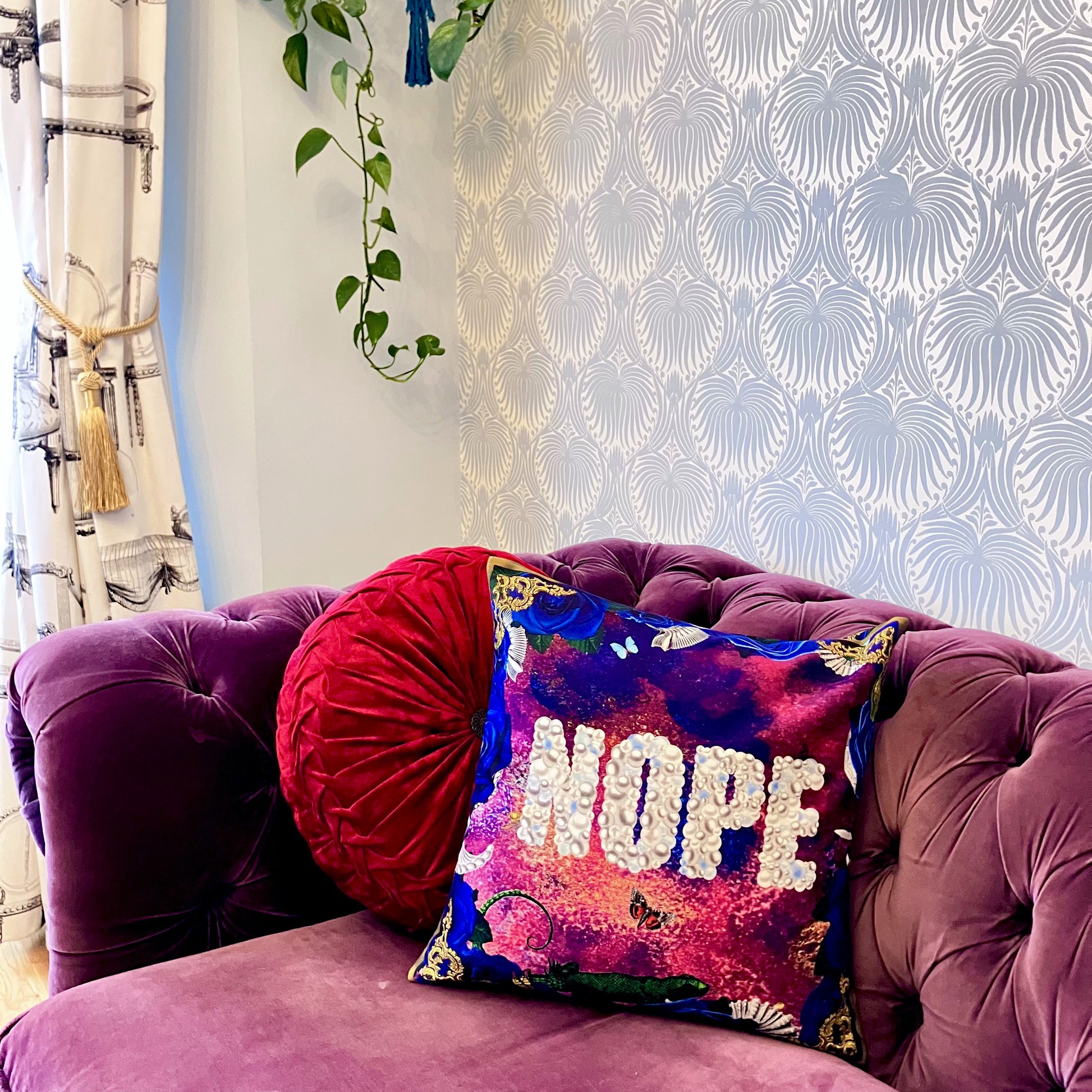 "Nope" Cushion Cover by House of Frisson. Featuring the word "Nope" written with pearls, framed by blue roses, and shells, against a blue and purple background. Showing cushion on a sofa in a room.