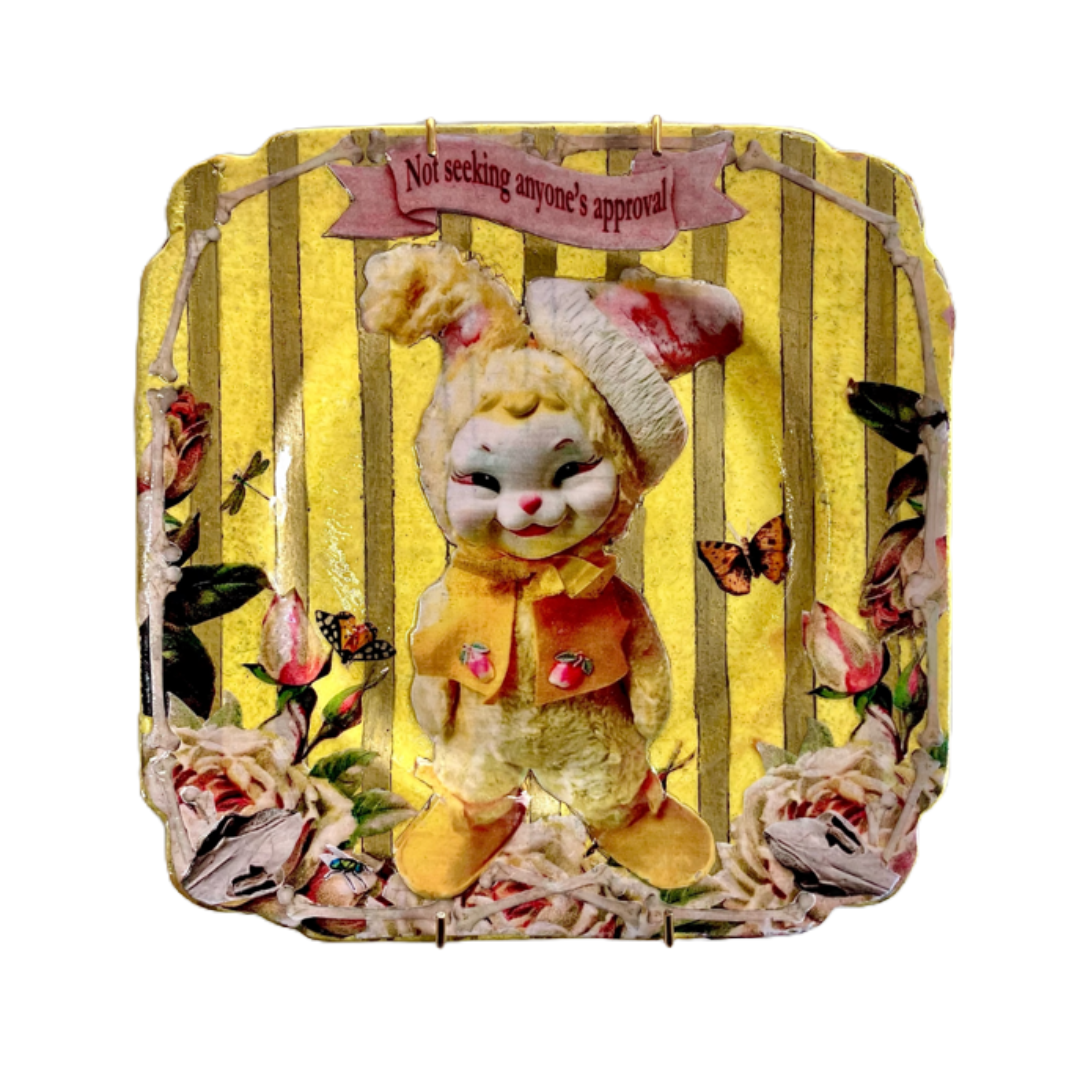 "Not Seeking Anyone's Approval" Wall Plate by House of Frisson, featuring a collage artwork of a kitsch vintage bunny framed by roses, moths, and bones, on a yellow and gold background.