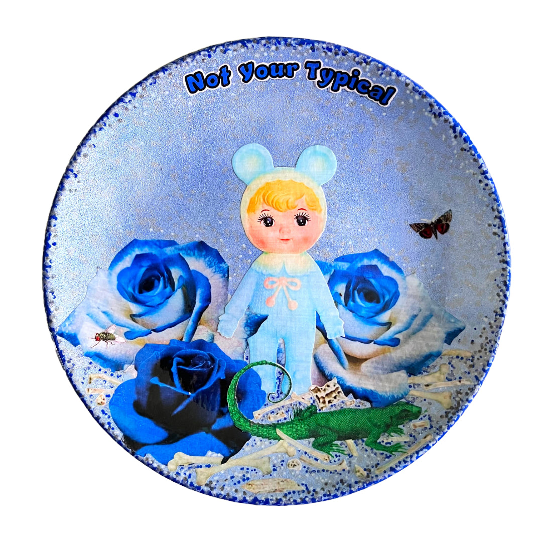 Light Blue Wall Plate by House of Frisson, featuring a kitschy vintage rubber doll surrounded by blue roses, with scattered bones, a lizard, and a fly. Guaranteed to bring a dose of fun and personality to your space! 