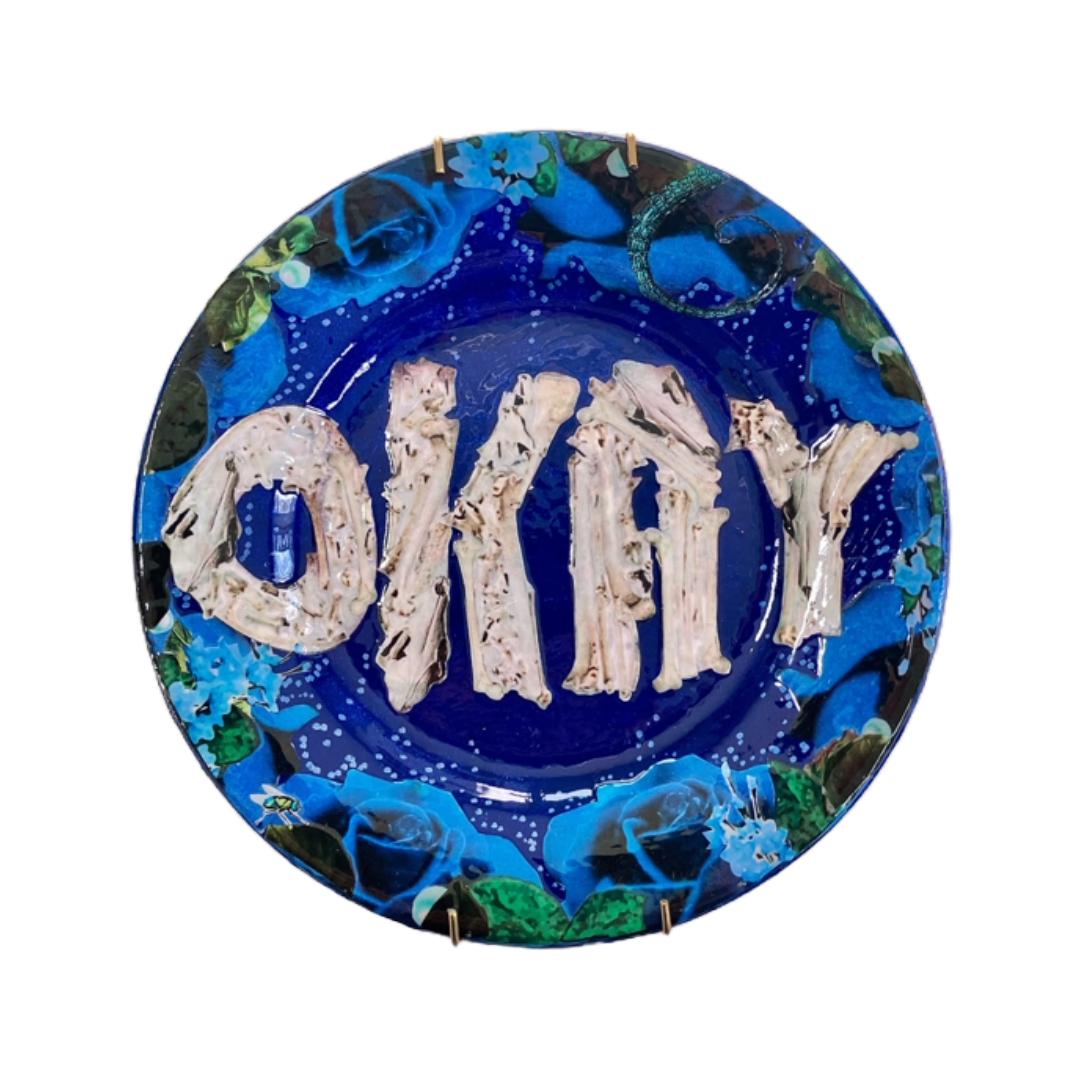 House of Frisson's "Okay" Wall Plate one-of-a-kind collage artwork on up-cycled plate. Featuring the word "Okay" written with bones, framed with blue roses, on a blue background.