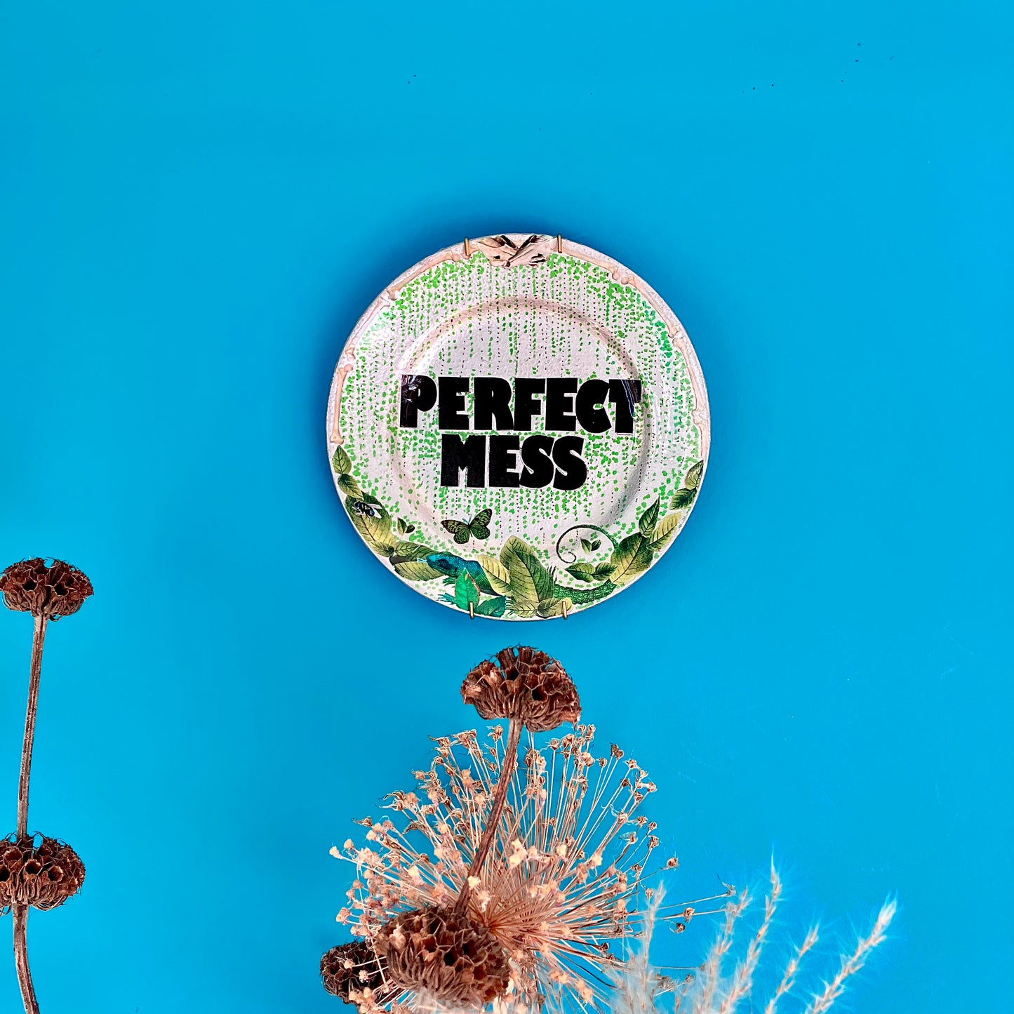 "Perfect Mess" Wall Plate by House of Frisson, hanging on a blue wall.