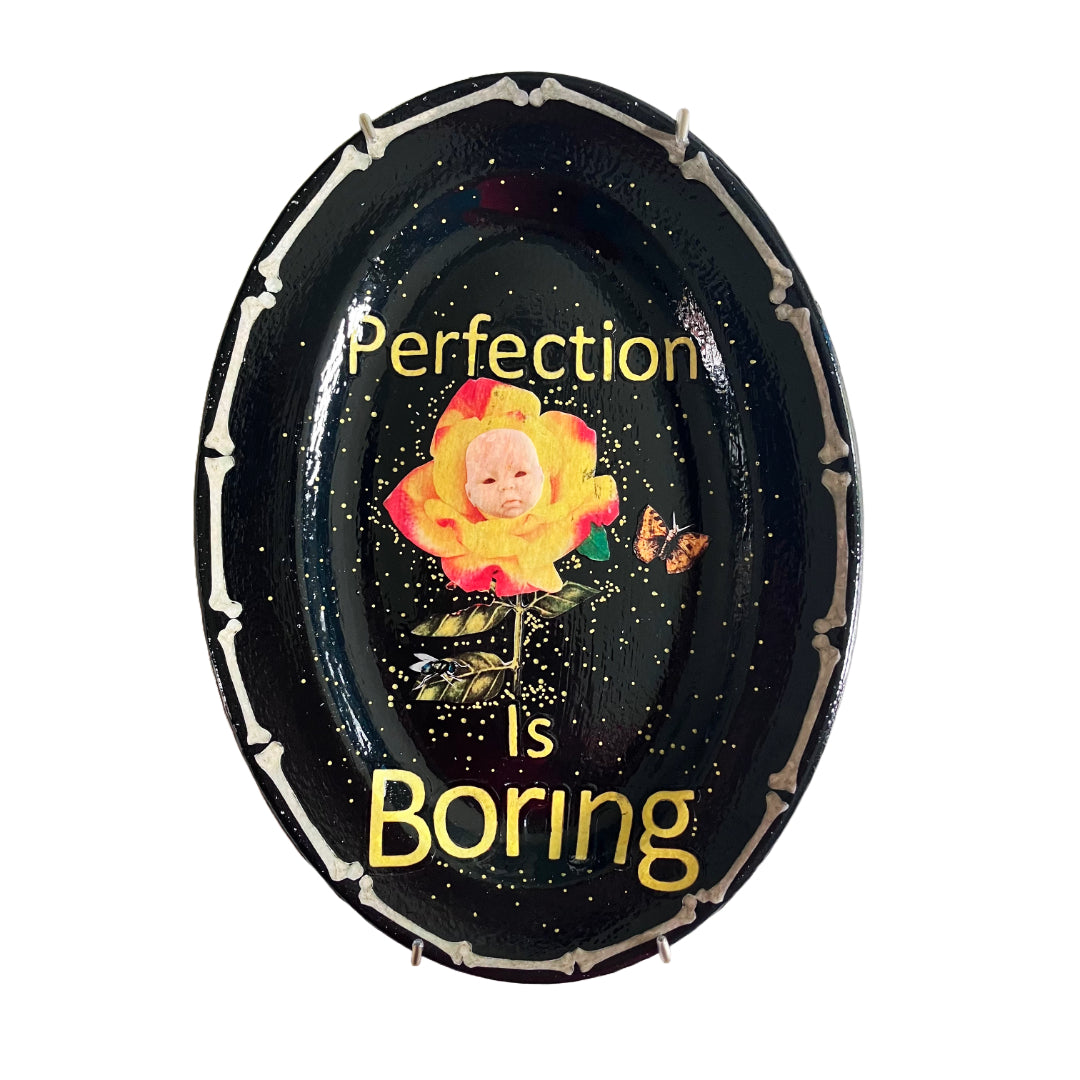 "Perfection Is Boring" Upcycled Wall Plate by House of Frisson, featuring a collage of a yellow rose with a doll face, a moth, and House of Frisson's fly, in a frame of bones.