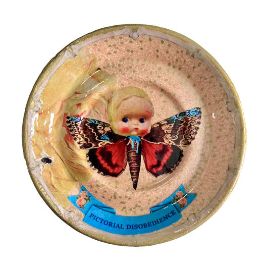 "Pictorial Disobedience" Trinket Dish by House of Frisson. Featuring a moth with doll head, framed by bones, on a beige background.