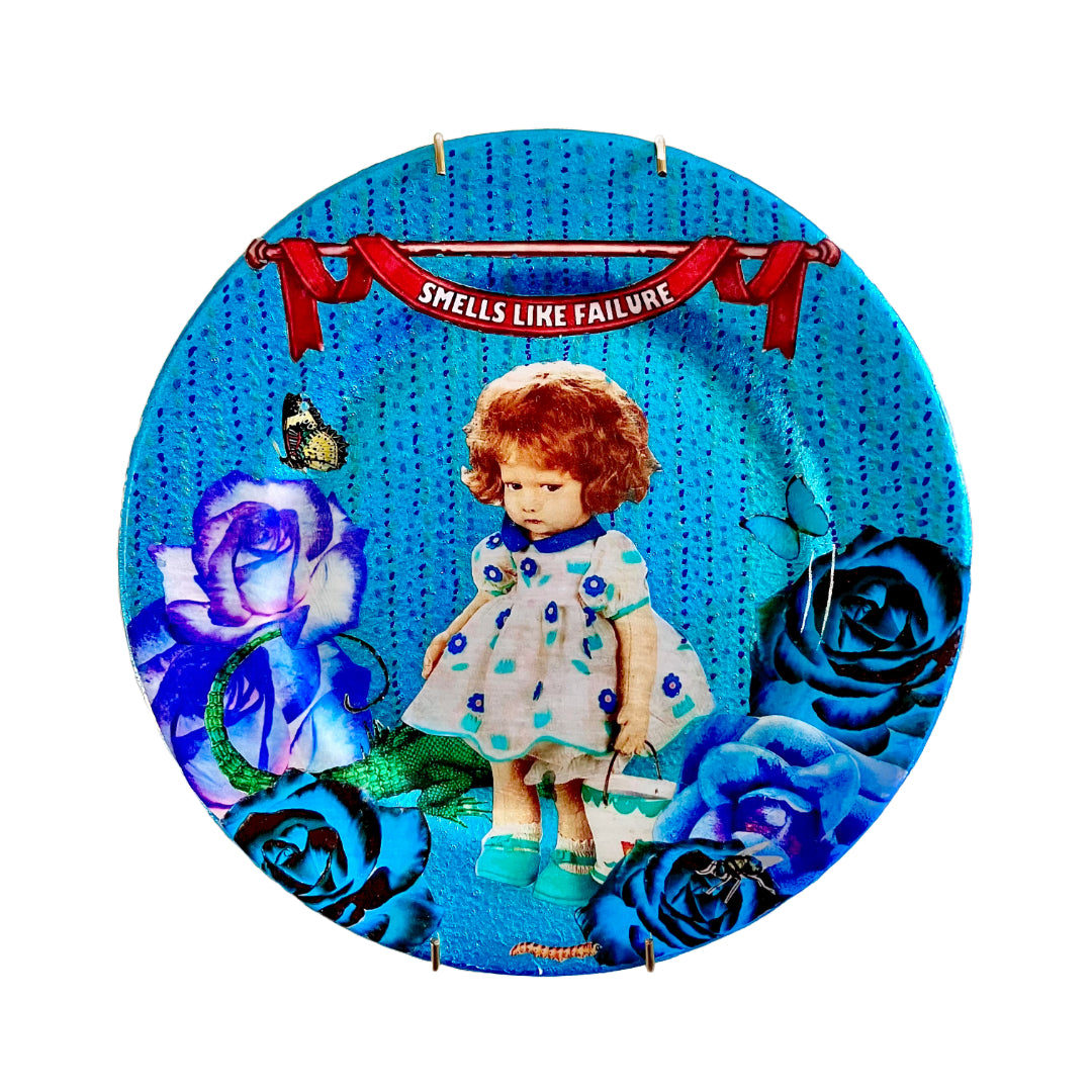 "Smells Like Failure" Wall Plate by House of Frisson, featuring a collage artwork of a vintage doll surrounded by blue roses, moths, and a lizard, set on a metallic blue background.