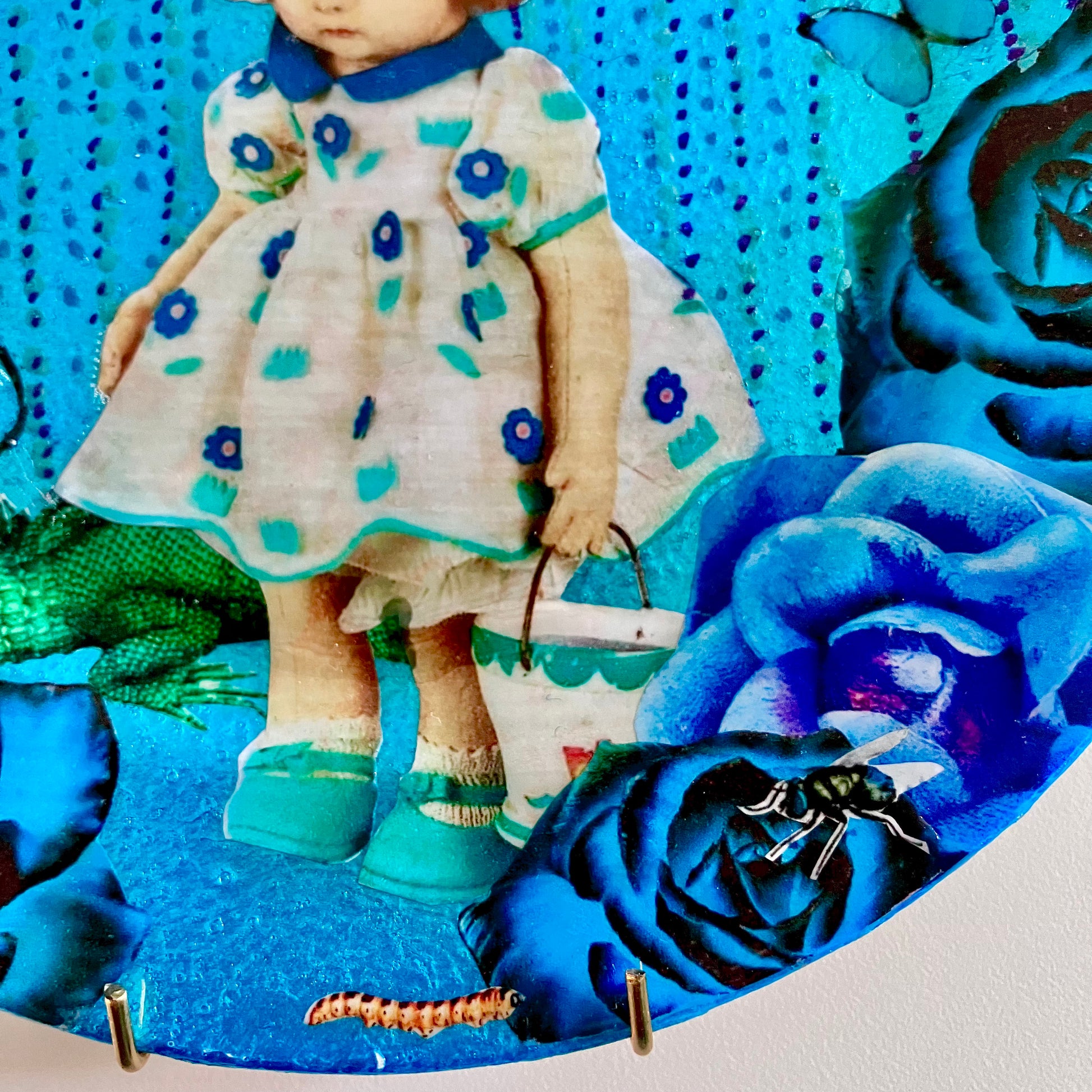 "Smells Like Failure" Wall Plate by House of Frisson, closeup detail of the collage showing a vintage doll, a lizard, and blue roses.
