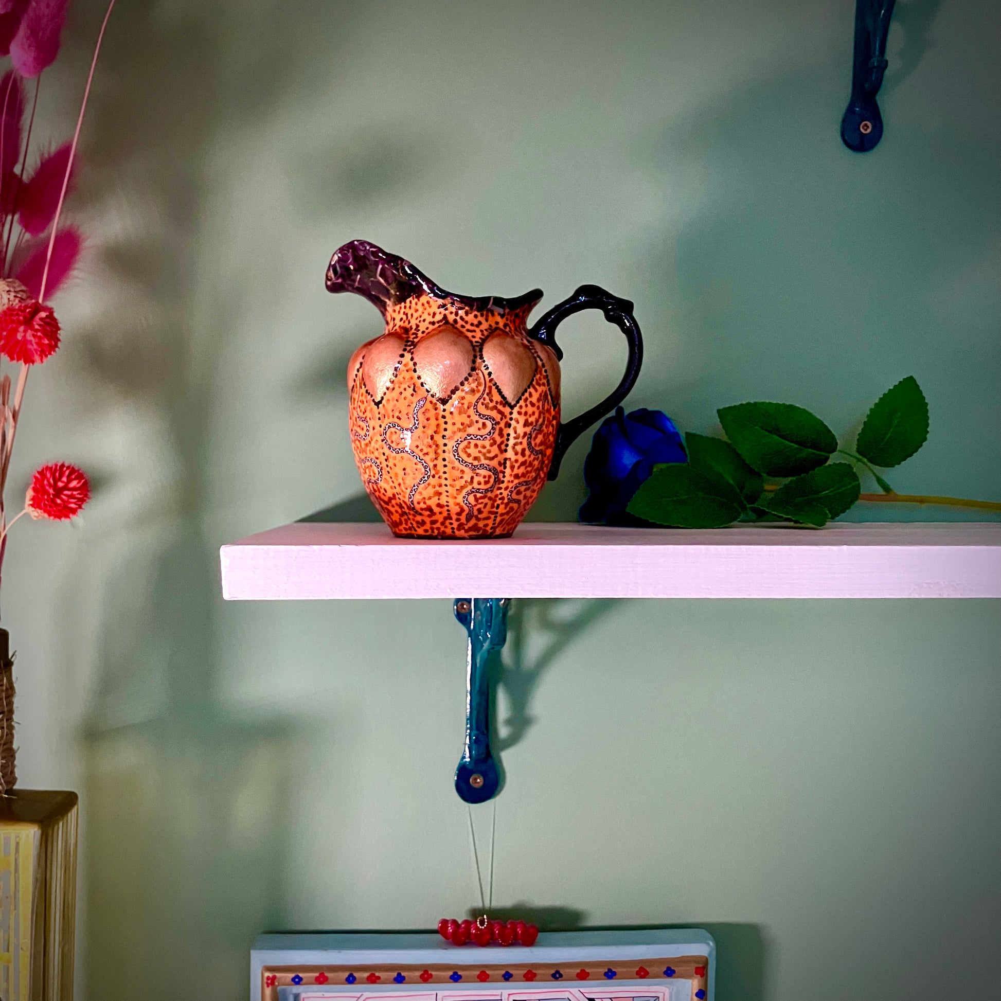 Orange and black upcycled jug/vase by House of Frisson, featuring a collage of snakes against an orange background with black accent. Vase resting on a shelf.