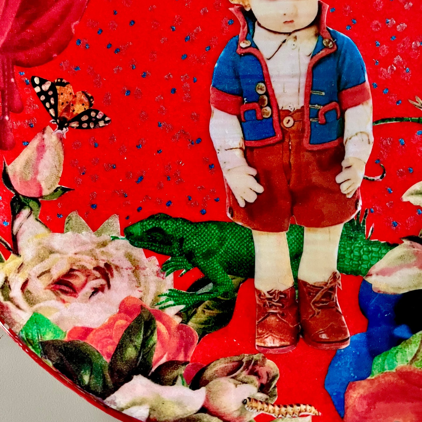 "Stop Making Sense" Wall Plate by House of Frisson,closeup detail of the collage showing a felt male doll, roses, and a lizard, against a red background.