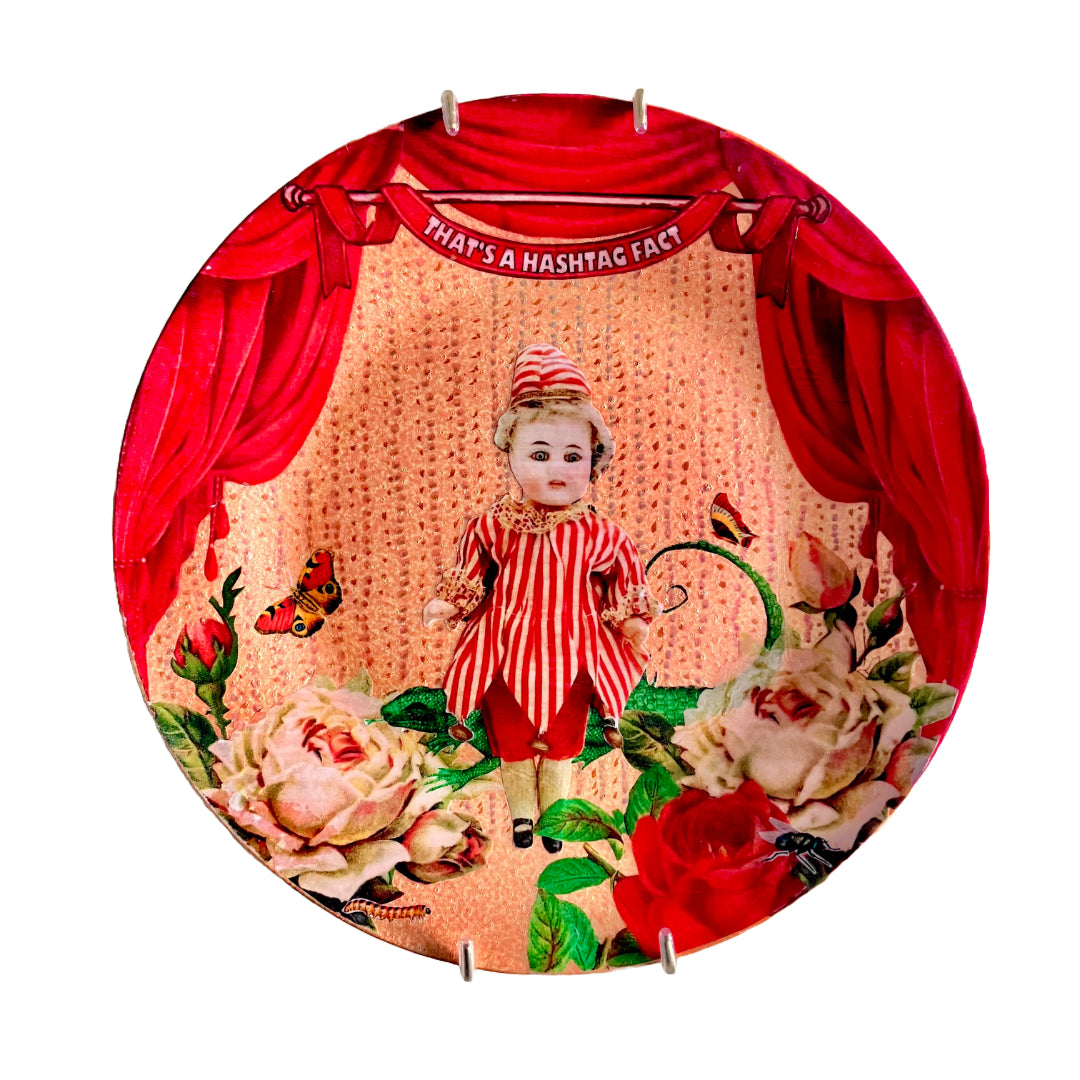 "That's A Hashtag Fact" Wall Plate by House of Frisson, featuring a felt doll dressed in pierrot, surrounded by roses, moths, and a lizard, framed by red curtains on a peach colour background.