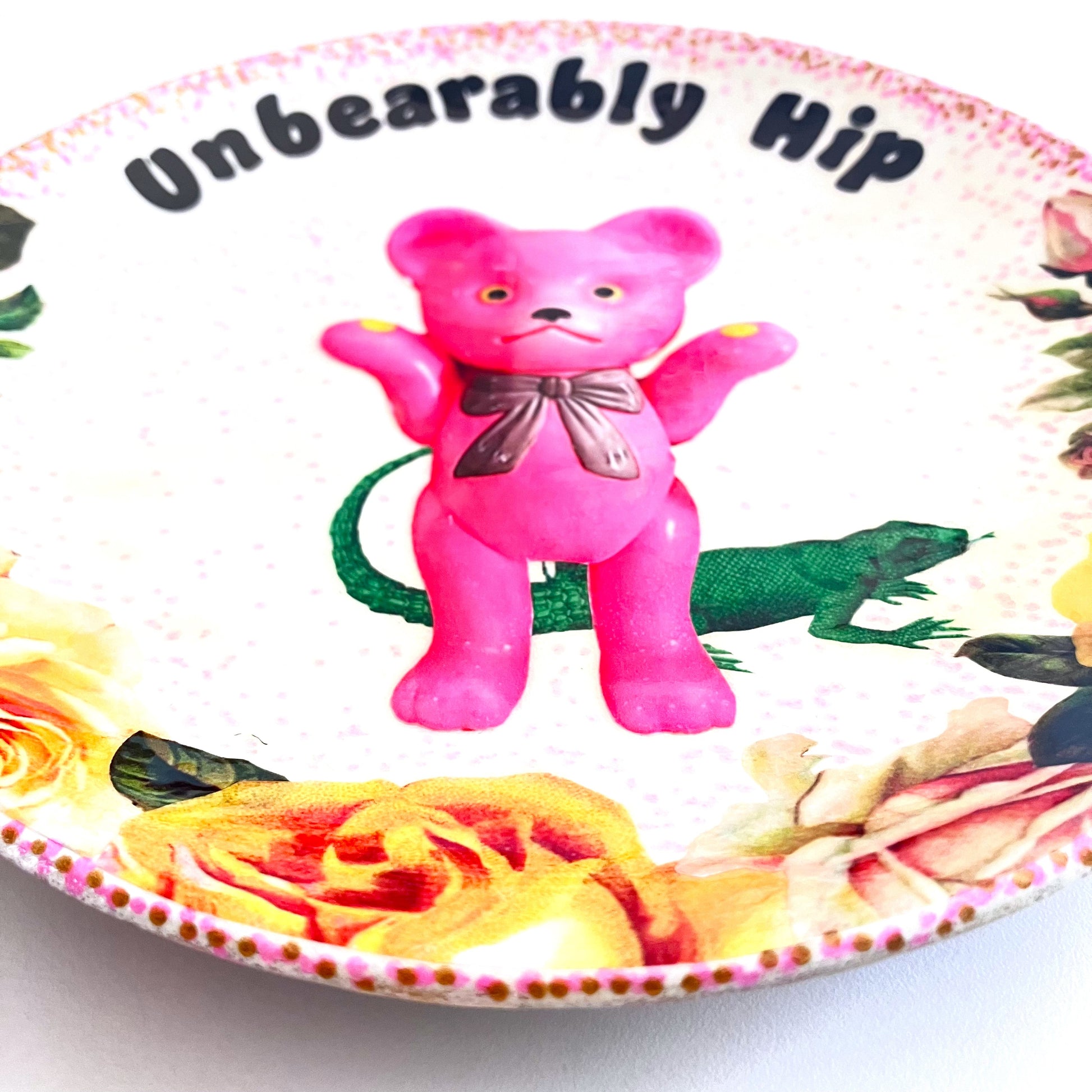 White Upcycled Wall Plate featuring a kitschy pink bear surrounded by whimsical creatures and roses, making it "Unbearably Hip." Closeup details of the collage.