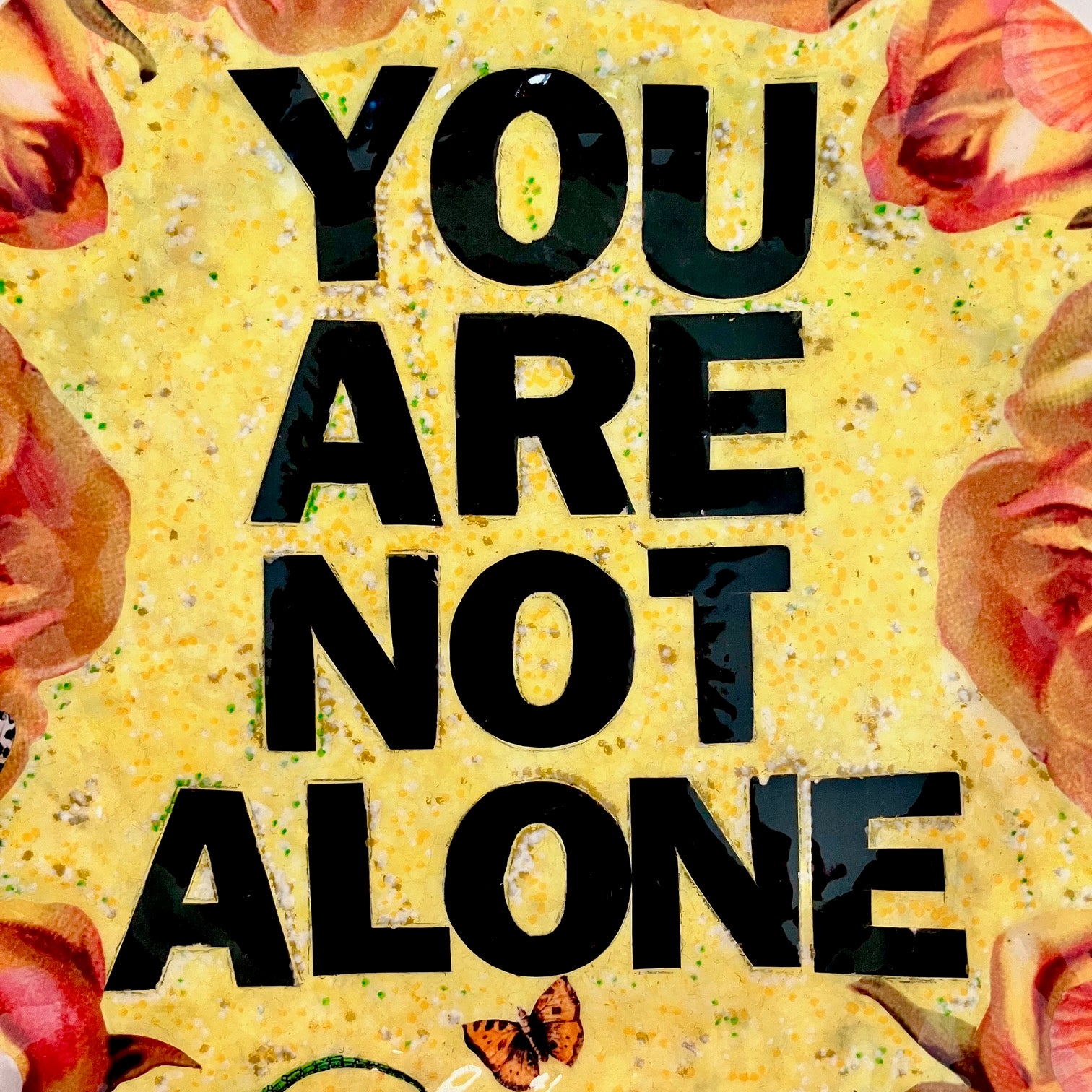"You Are Not Alone" one-of-a-kind collage artwork Wall Plate by House of Frisson. Featuring the words "You Are Not Alone" framed by roses, pearls, and moths, on a yellow background. Closeup details.