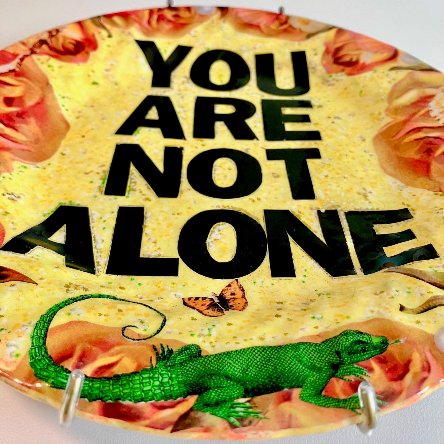 "You Are Not Alone" one-of-a-kind collage artwork Wall Plate by House of Frisson. Featuring the words "You Are Not Alone" framed by roses, pearls, and moths, on a yellow background. Closeup detail.