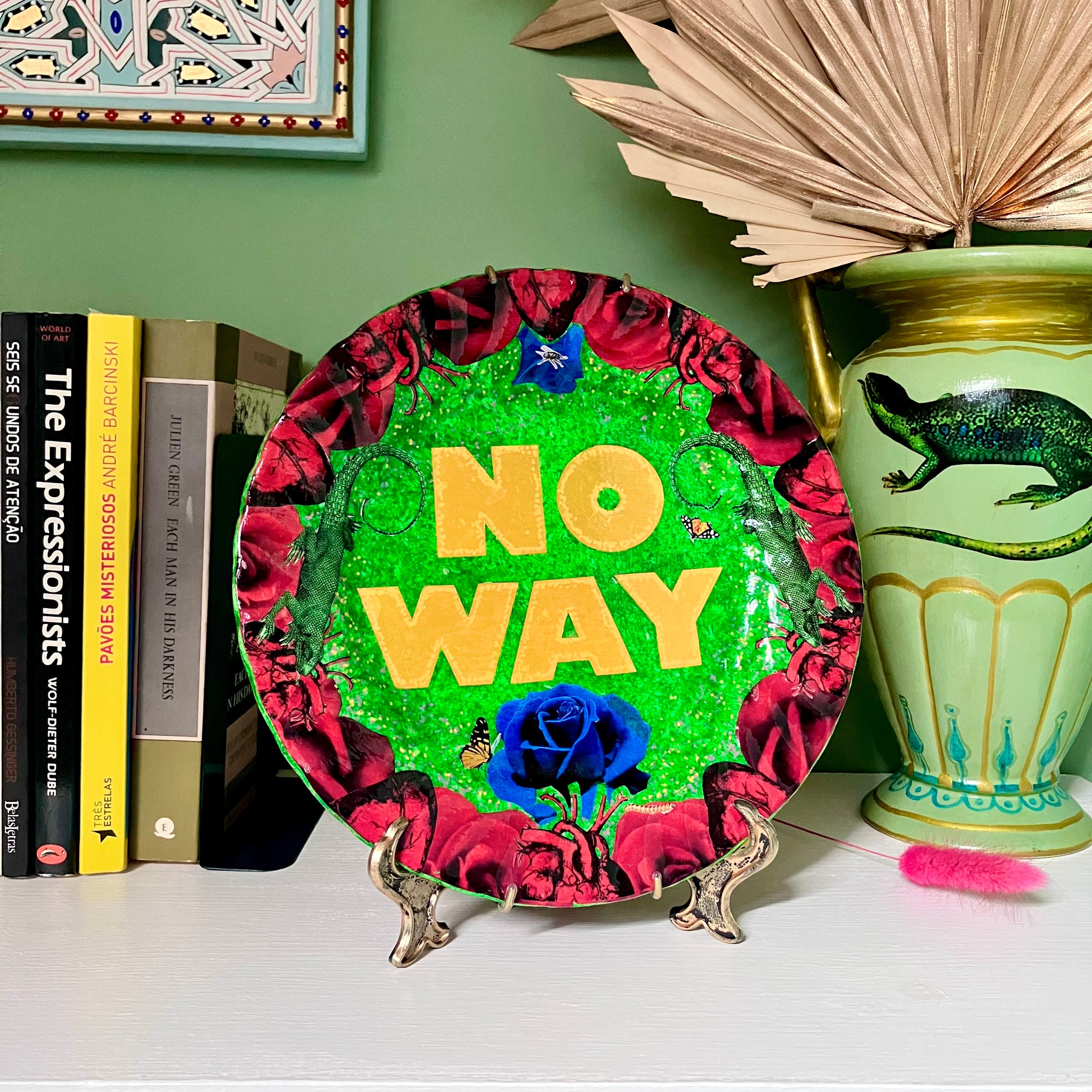 "No Way" one-of-a-kind collage artwork on upcycled wall plate by House of Frisson. Featuring the words "No Way" framed with a collage of roses, and lizards, on a green background. Lifestyle image showing plate on a plate stand resting on a shelf.