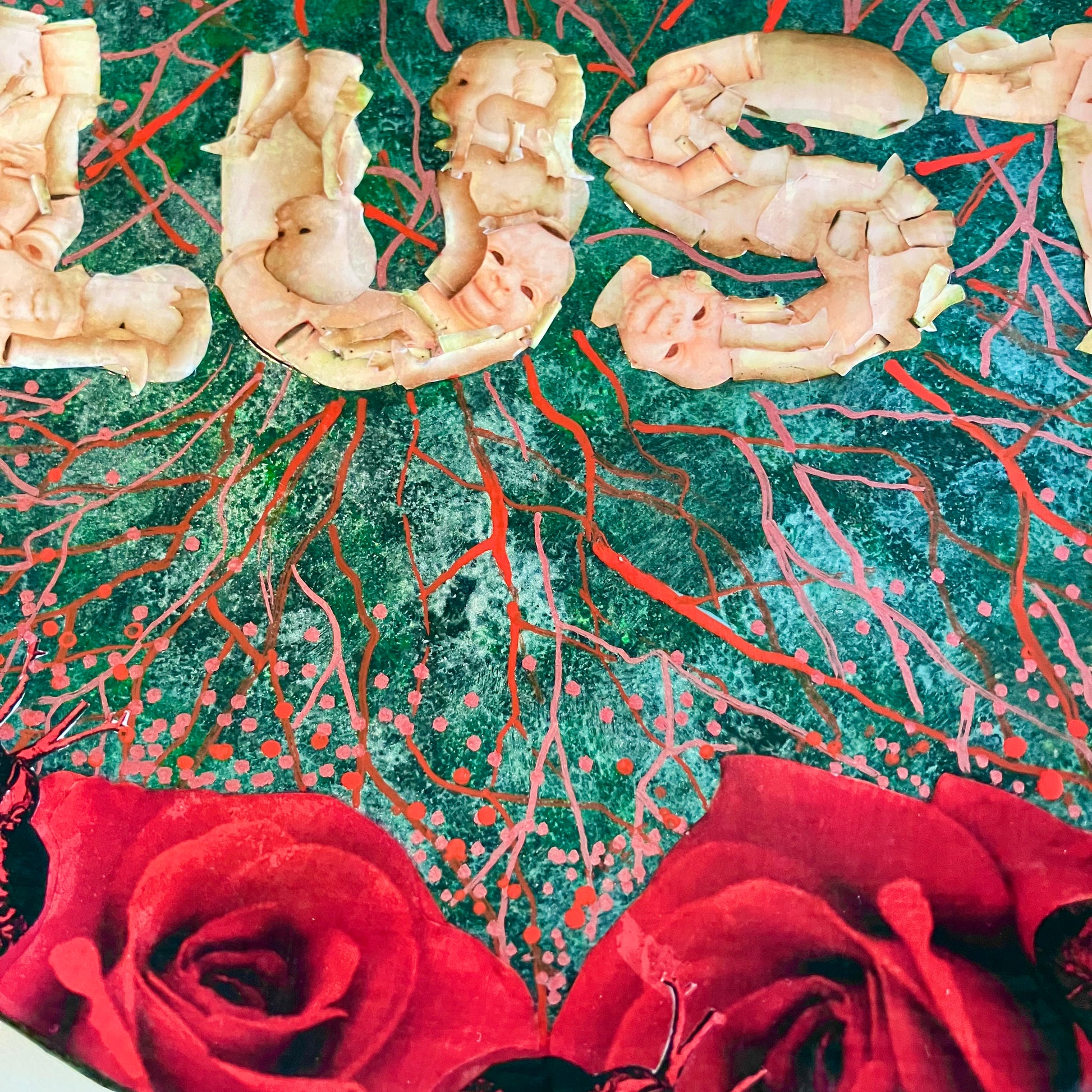 "Lust" Wall Plate by House of Frisson, featuring the word "lust" written with plastic doll parts, framed by red roses and anatomical human heart ,on a charcoal grey background with vein patterns. Closeup detail .