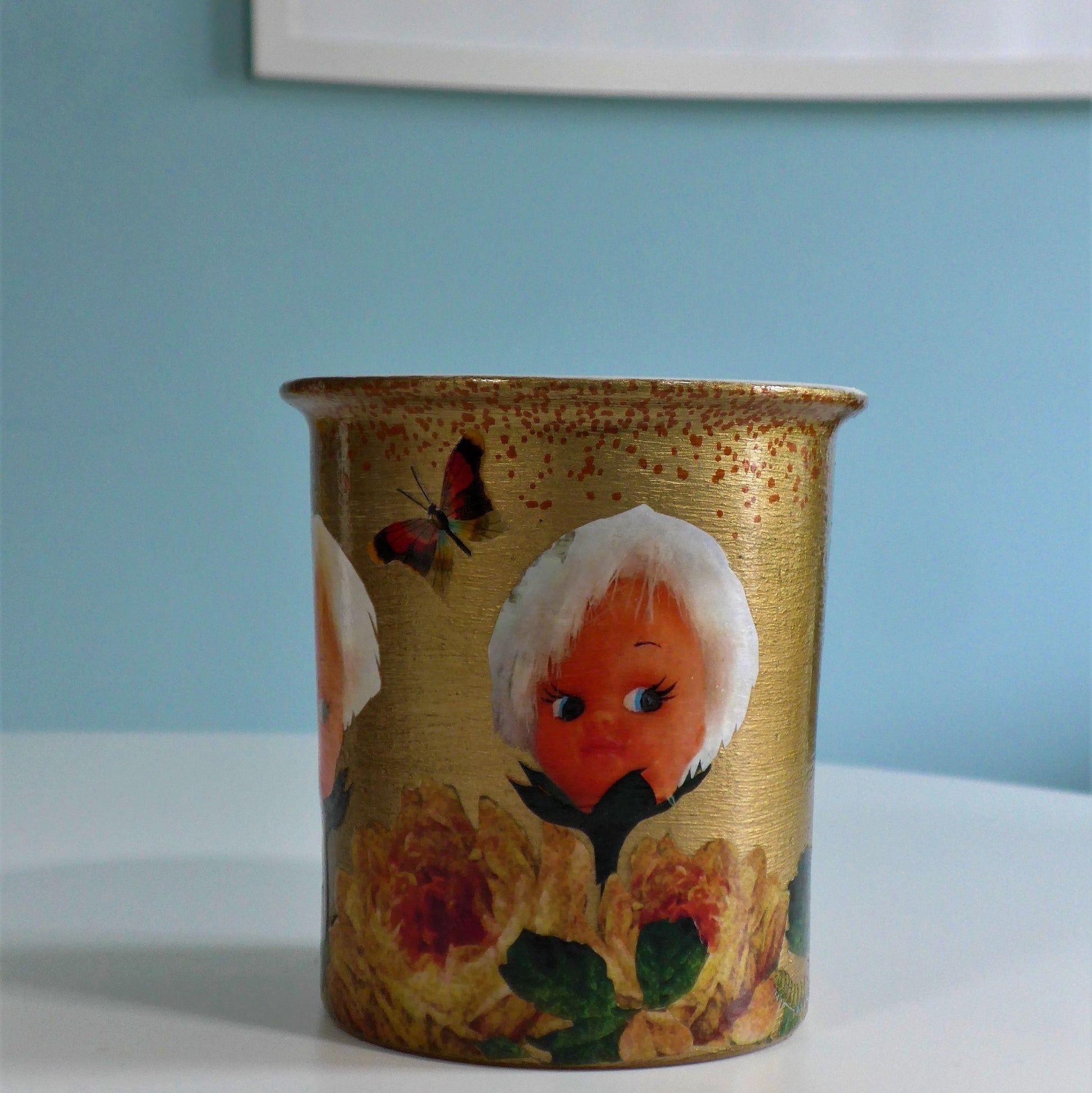 House of Frisson "Doll Face" Gold Plant Pot Flower Vase Front. Featuring flowers with doll heads, and moths, on a golden background.