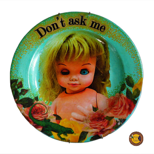 House of Frisson "Don't Ask Me" Green Wall Plate Front. Collage artwork featuring a vintage doll with funny face, surrounded by roses, and a lizard.