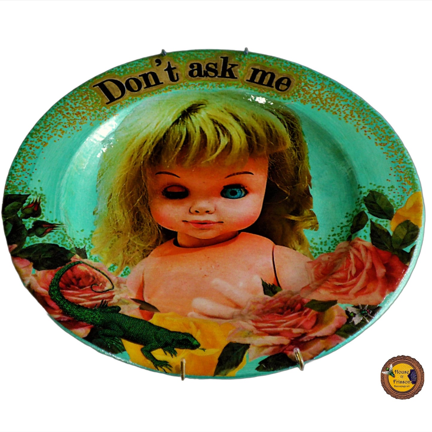 House of Frisson "Don't Ask Me" Green Wall Plate Front. Collage artwork featuring a vintage doll with funny face, surrounded by roses, and a lizard. Closeup details.
