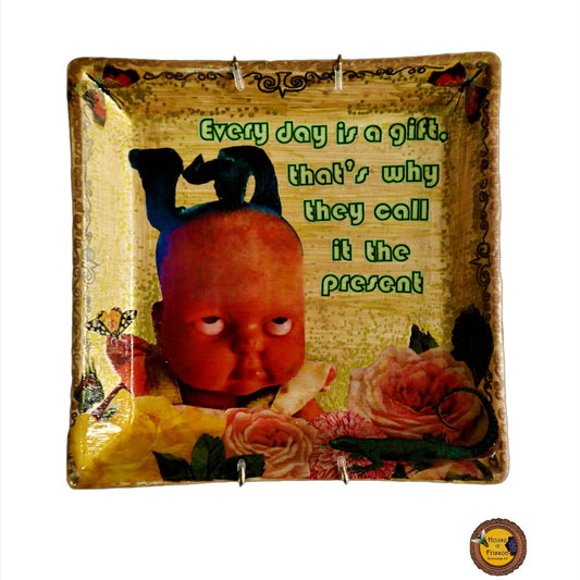 House of Frisson "Every Day Is A Gift, That's Why They Call It The Present" Beige Wall Plate. Collage artwork on upcycled plate, featuring a doll rolling  eyes, flowers, and a lizard.